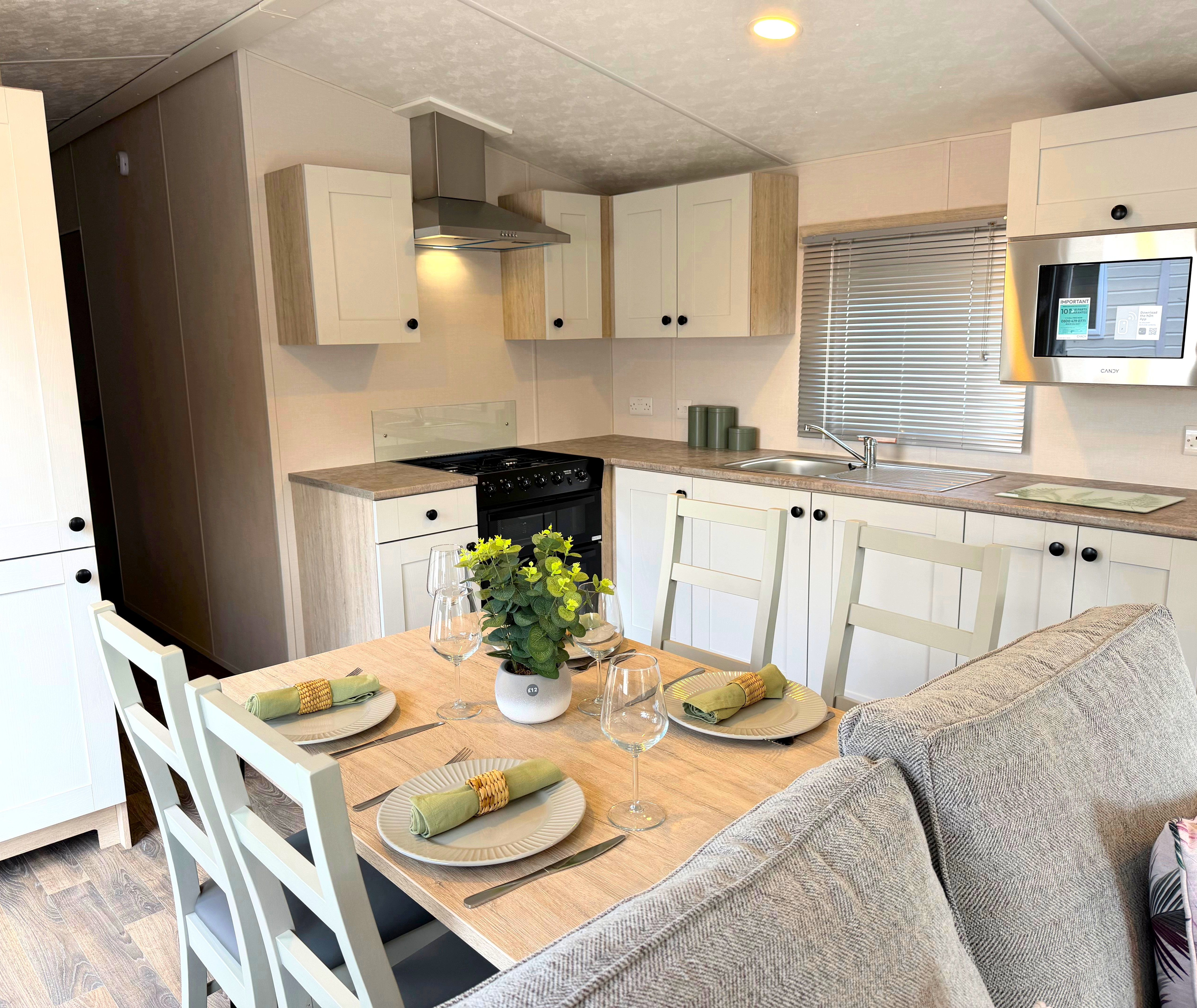 Delta Saffron kitchen area with white cupboards, integrated microwave, sink and dining table set for four