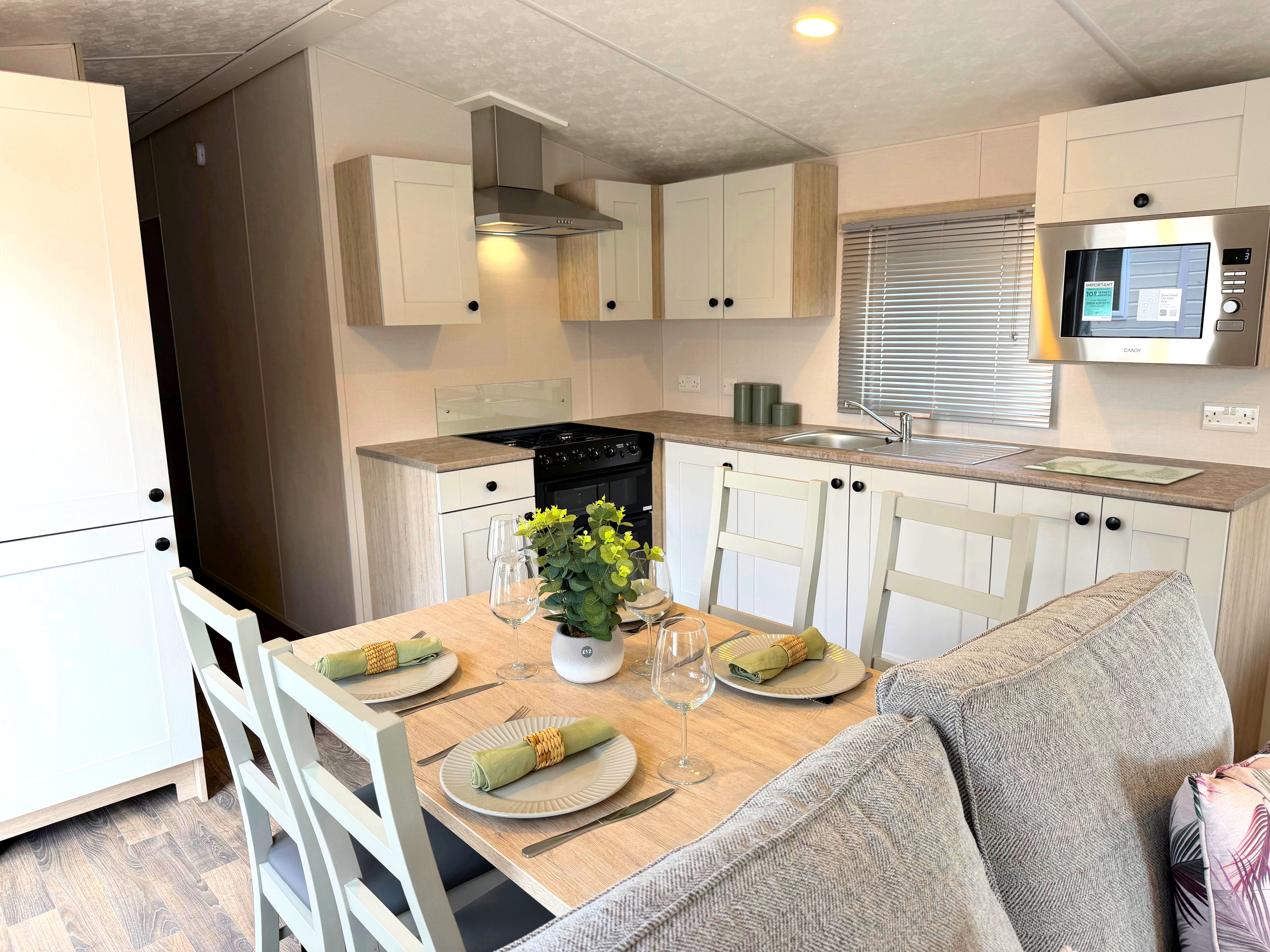 Delta Saffron kitchen area with white cupboards, integrated microwave, sink and dining table set for four