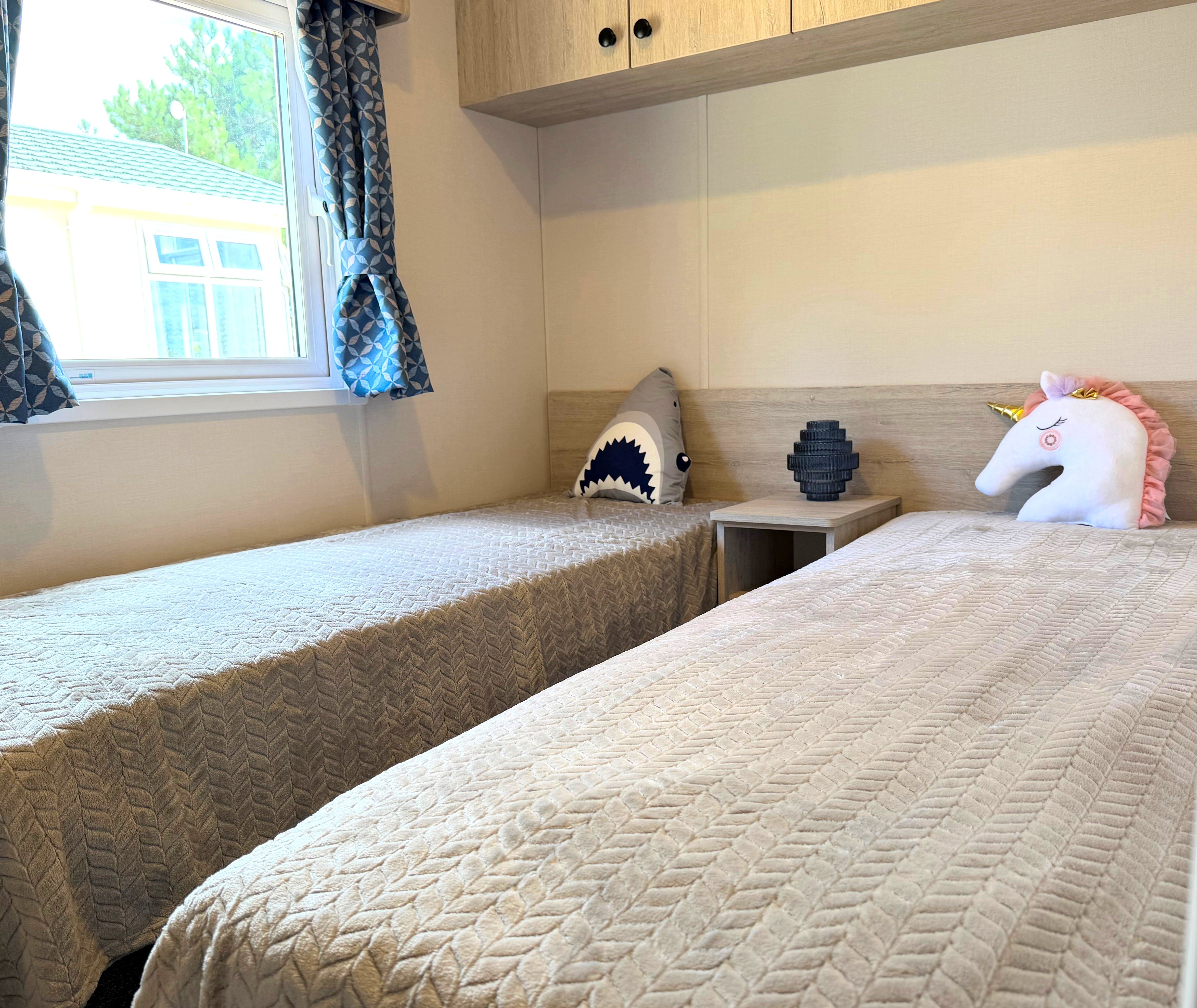 Delta Saffron twin bedroom with two single beds, patterned blue curtains and bedside table