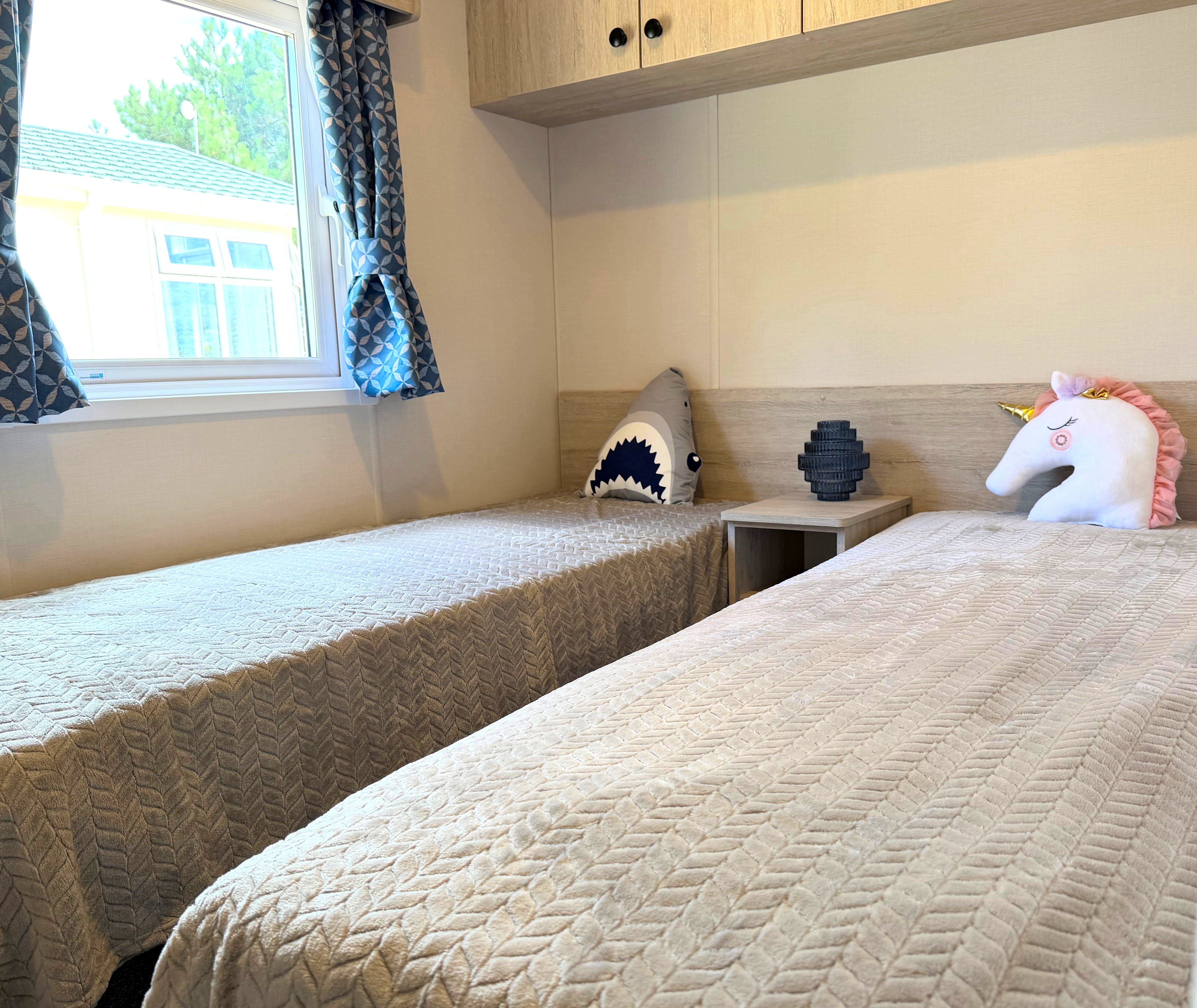 Delta Saffron twin bedroom with two single beds, patterned blue curtains and bedside table