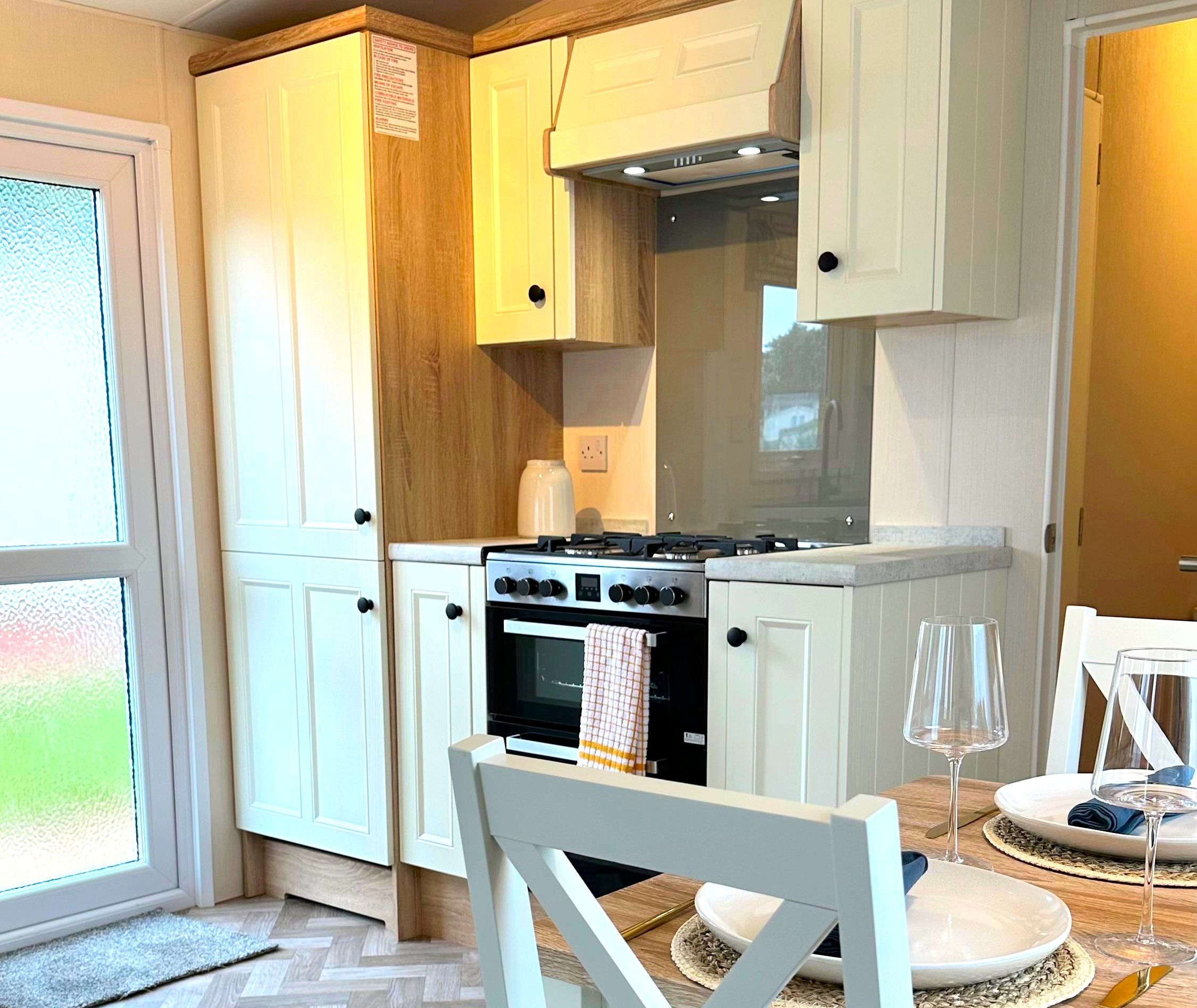 Kitchen Europa Willow Classic with cream shaker cabinets, oak trim and built-in oven beside a dining table set for two