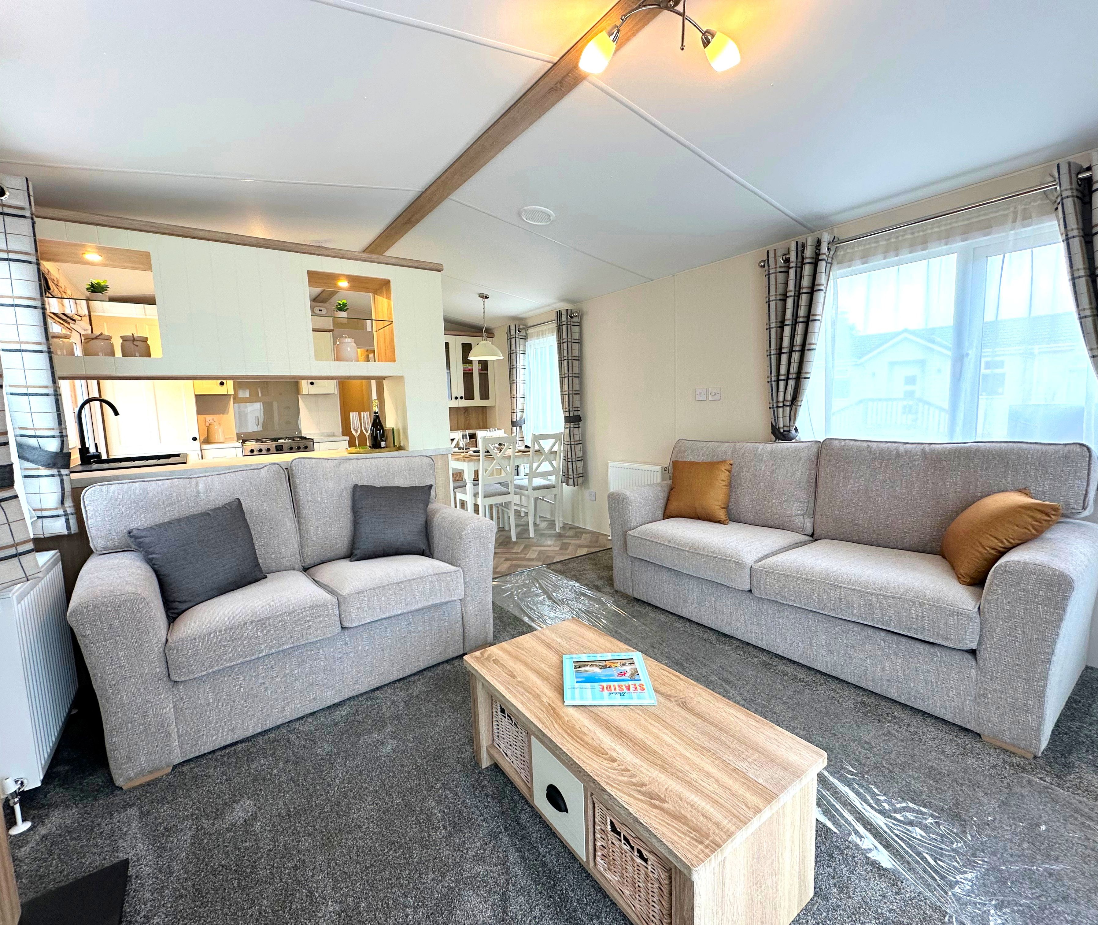 Bright open-plan living space with two grey sofas, wooden coffee table, and dining area beside a fitted kitchen