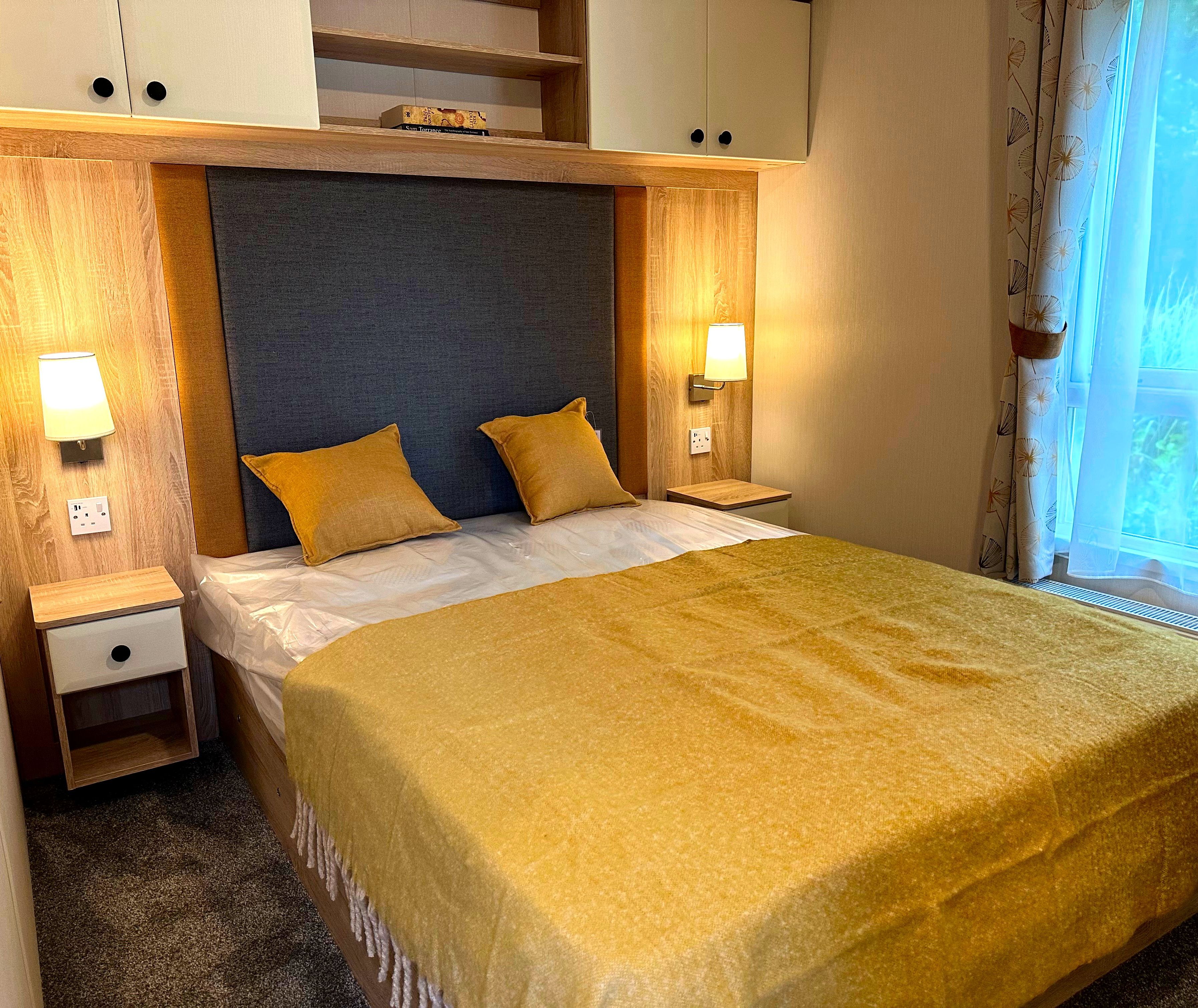 Cosy master bedroom with built-in headboard wall, bedside lights and mustard throw by the window