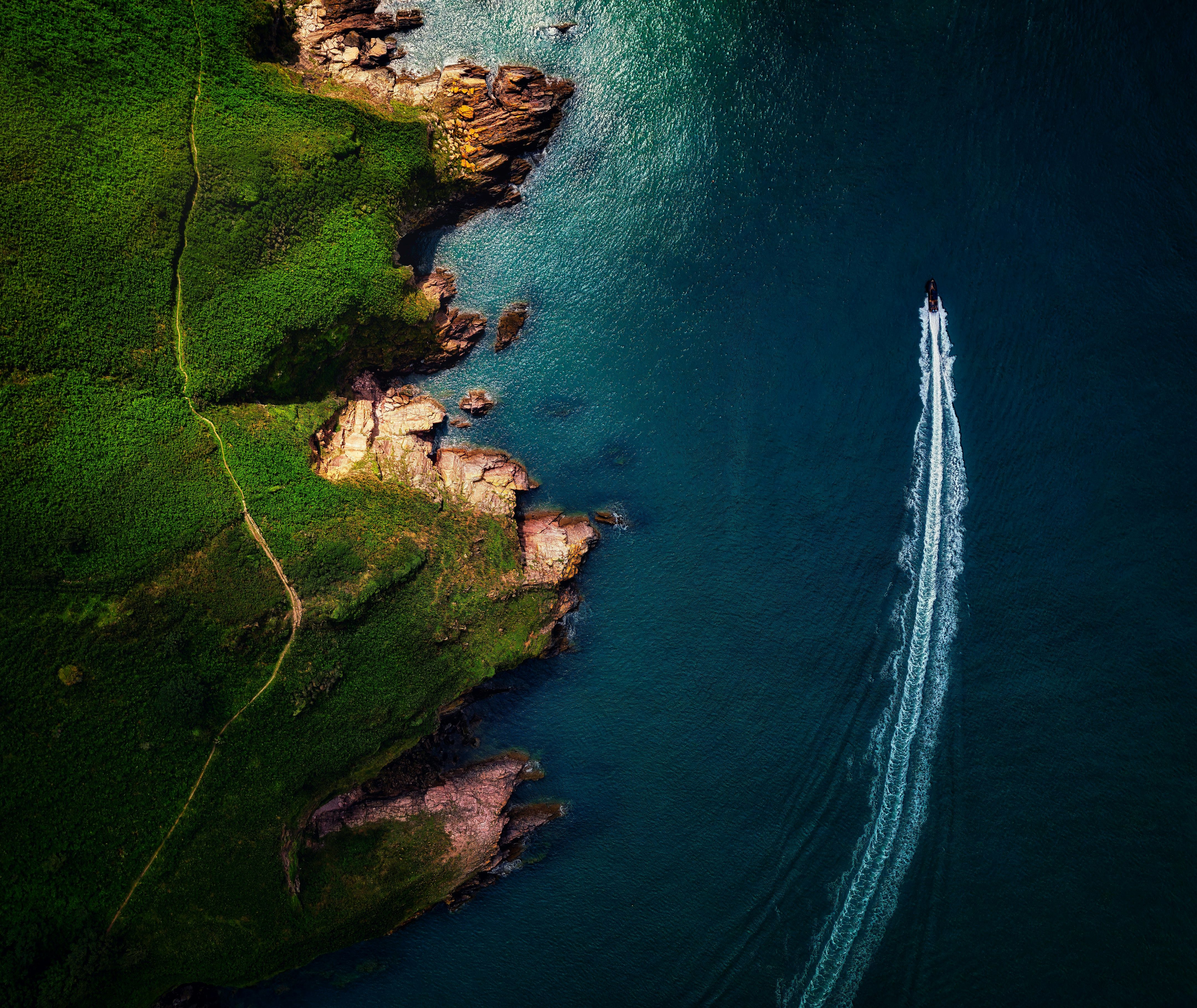 Aerial view of a speedboat leaving a white wake beside a rocky green coastline in deep blue water