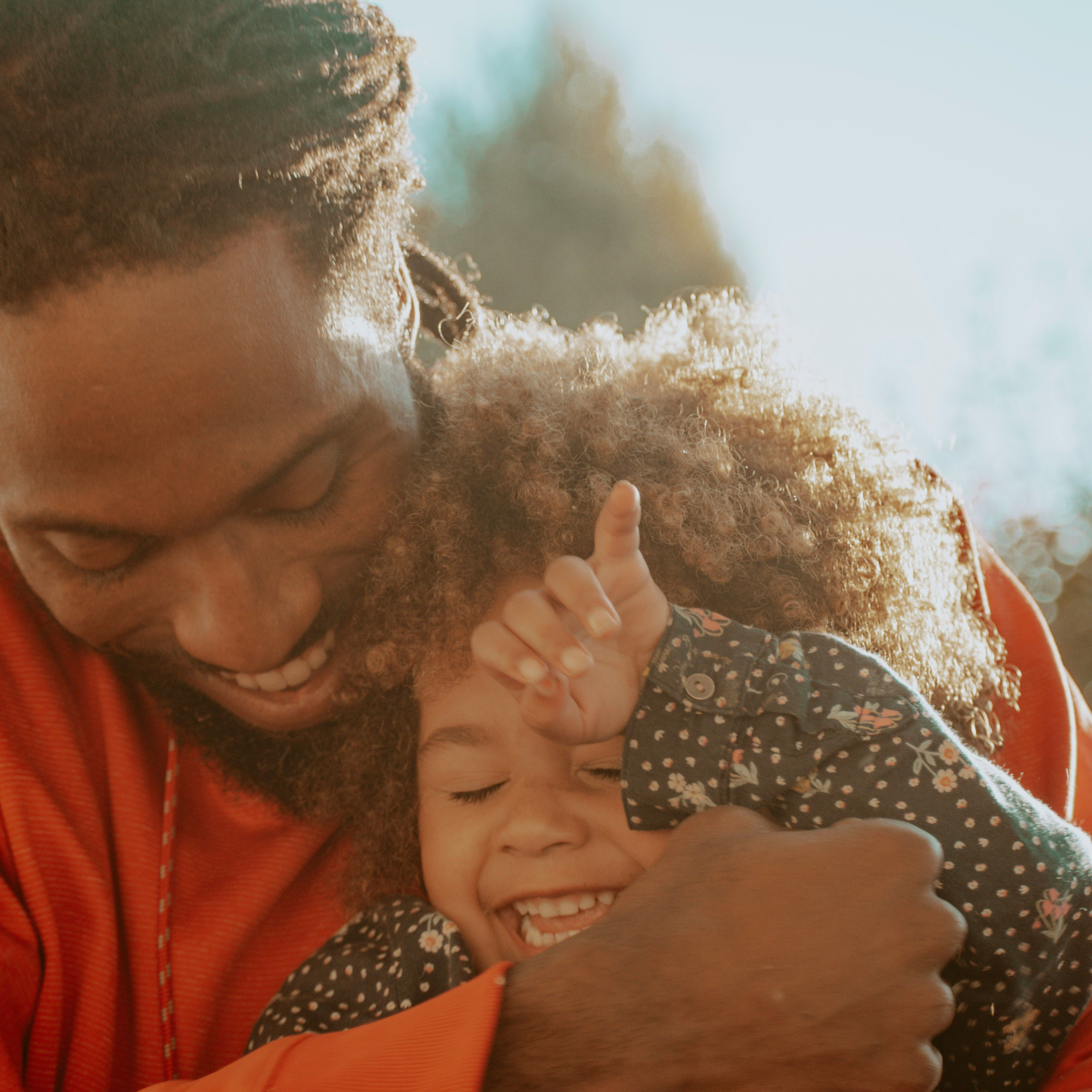 Adult hugging a laughing child outdoors in warm sunlight