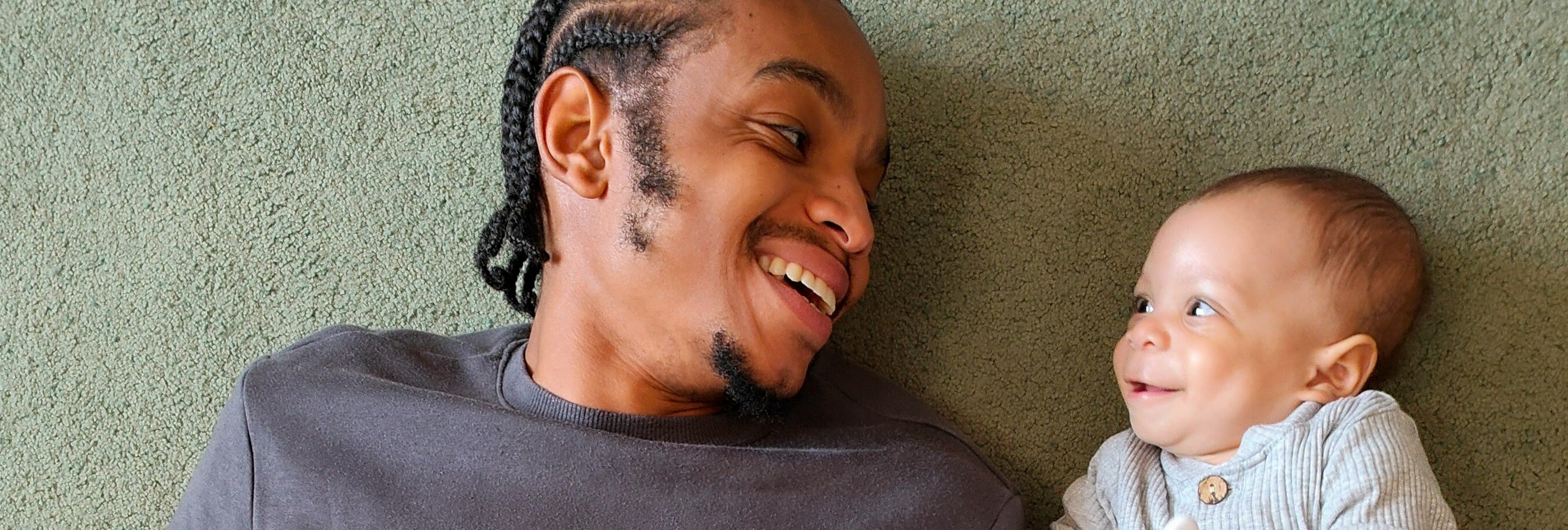 Father lying on a carpet smiling at his baby holding a spoon