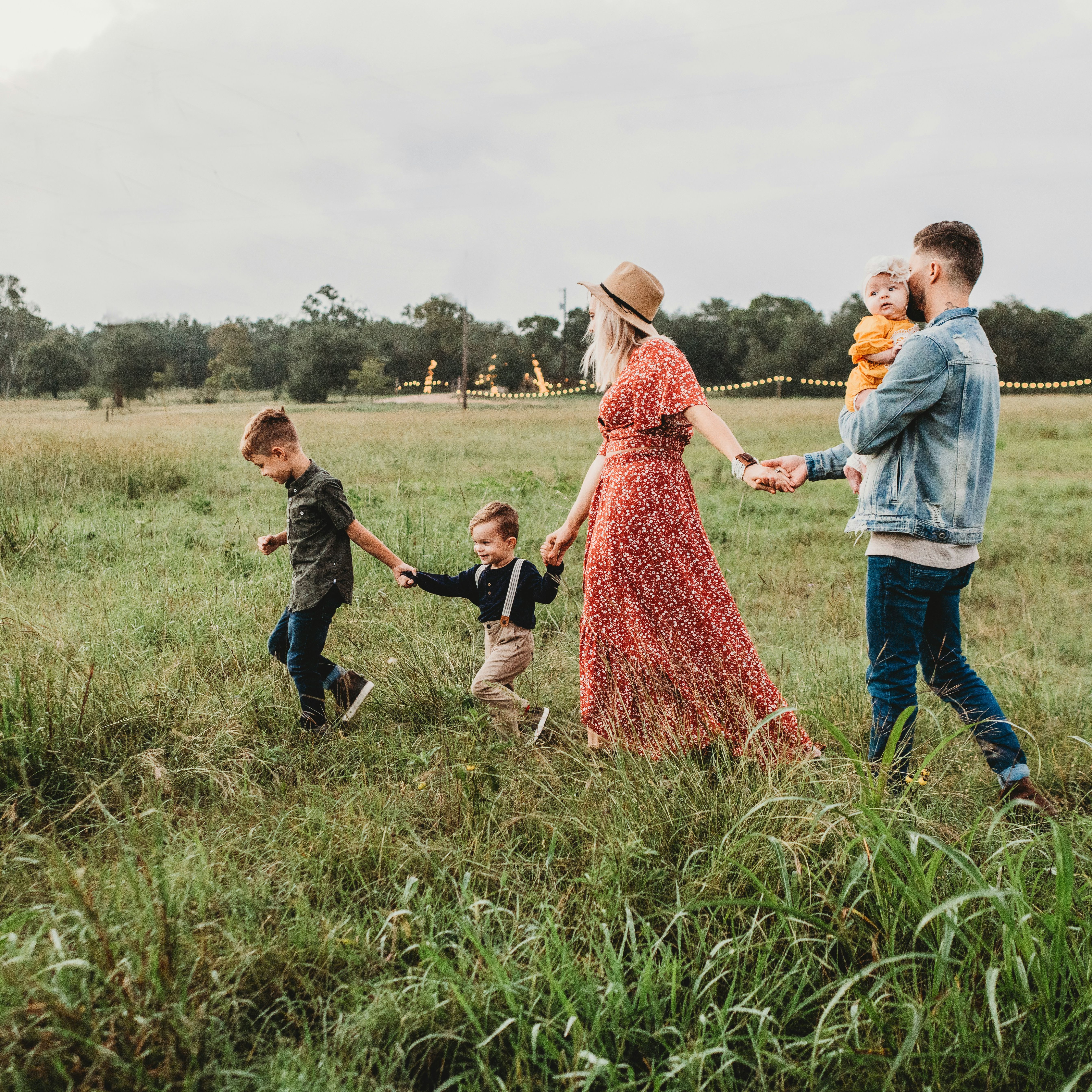 Family holding hands and walking through a grassy field at dusk