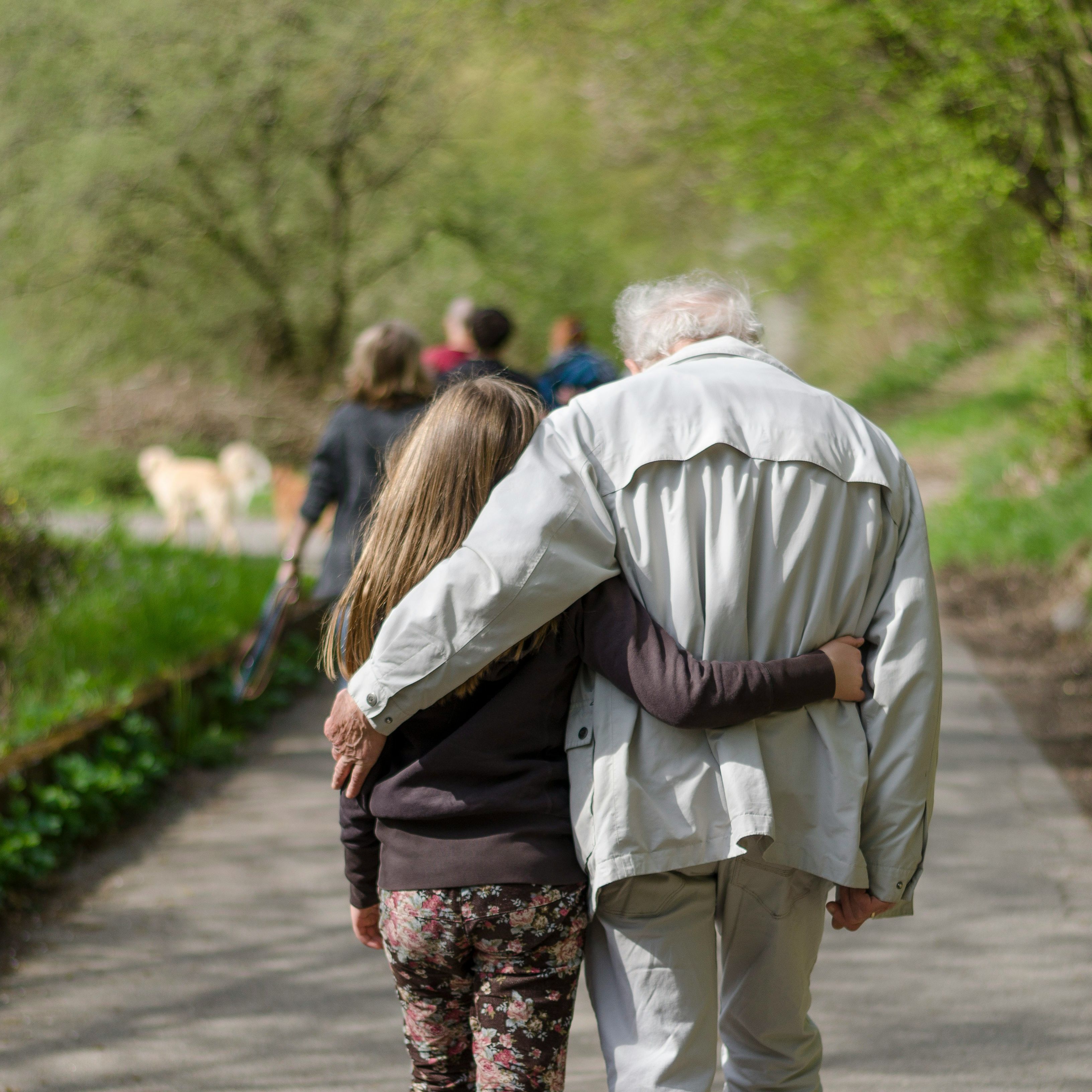 Elderly man and young girl walking arm in arm along a tree-lined path