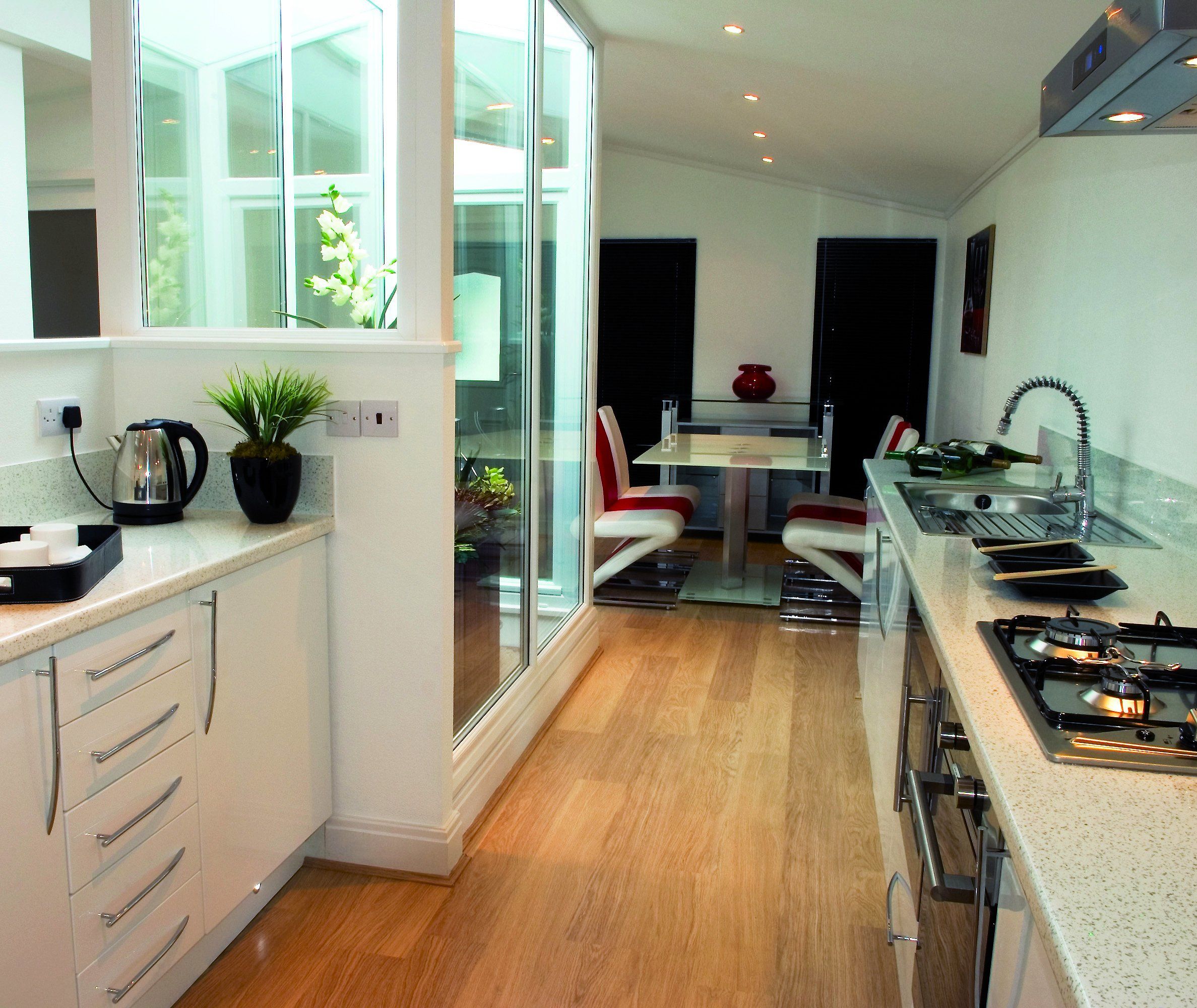 Modern galley kitchen with white cabinets, light worktops, gas hob and glass doors opening to a dining area