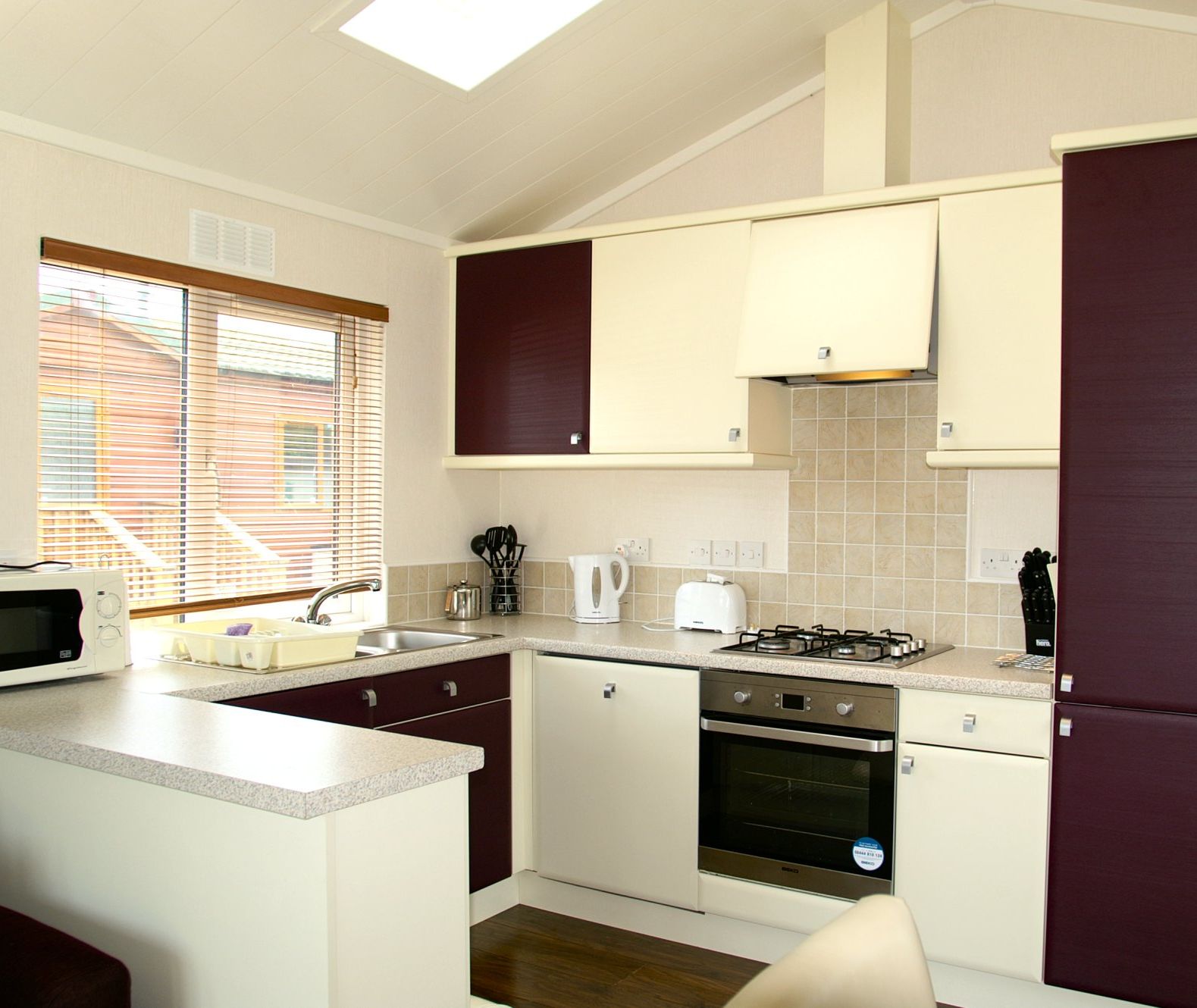 Modern fitted kitchen with cream and dark wood units, oven and gas hob, and a large window with blinds