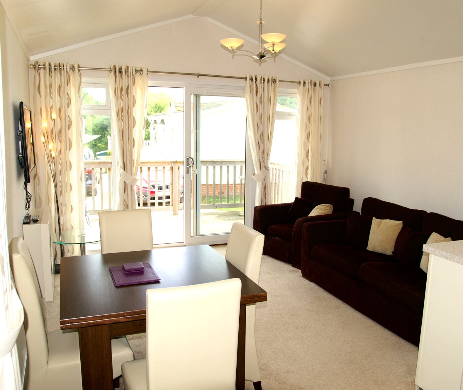 Bright open-plan living and dining area with dark sofas, dining table and sliding doors to a balcony
