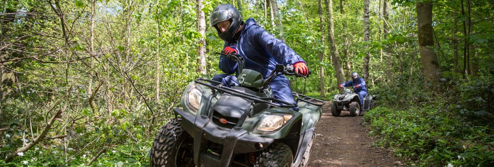 People riding quad bikes on a dirt trail through a forest.