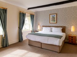 Cozy hotel room with double bed, two windows with blue curtains, bedside tables, and lamps.