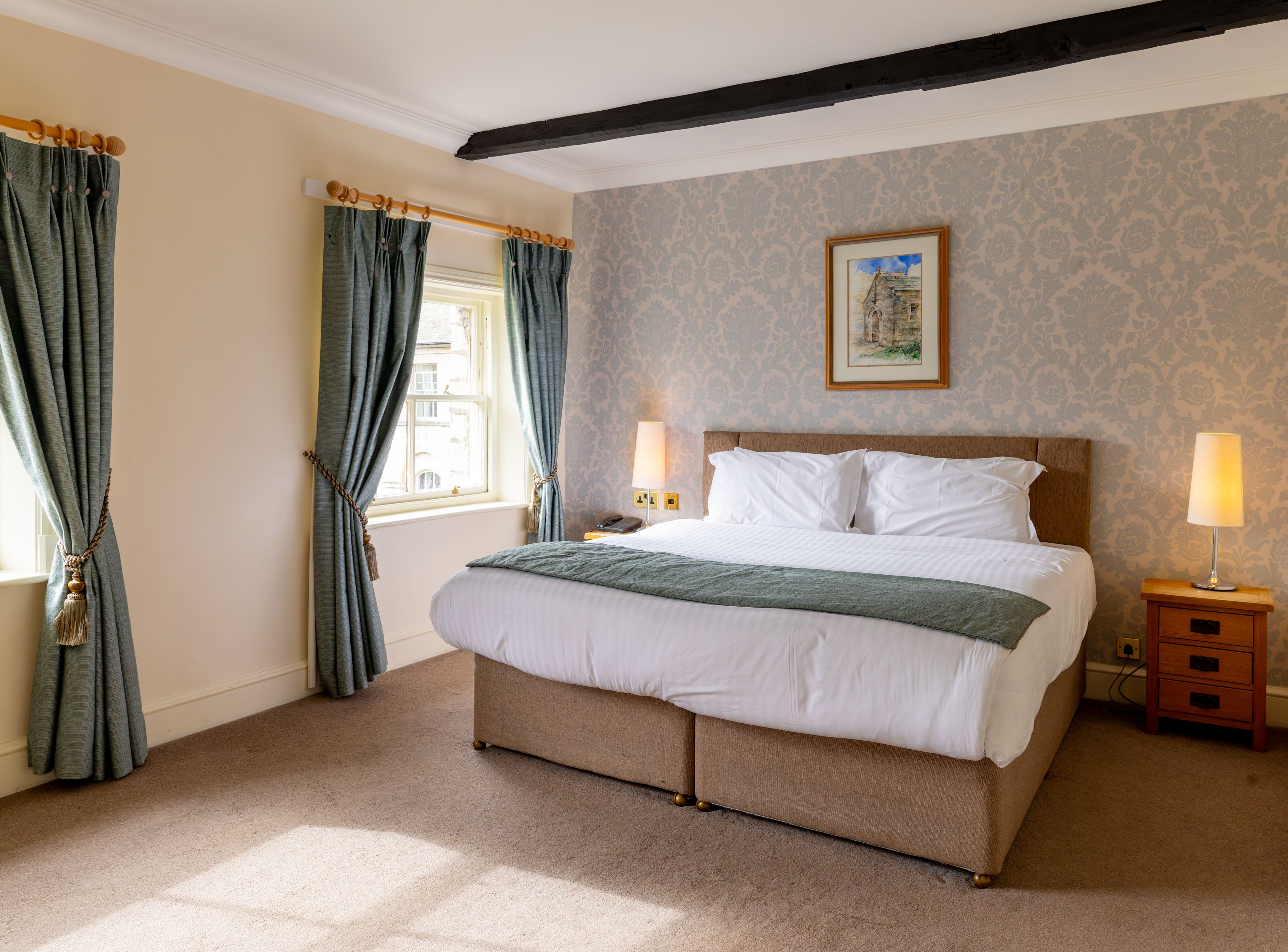 Cozy hotel room with double bed, two windows with blue curtains, bedside tables, and lamps.