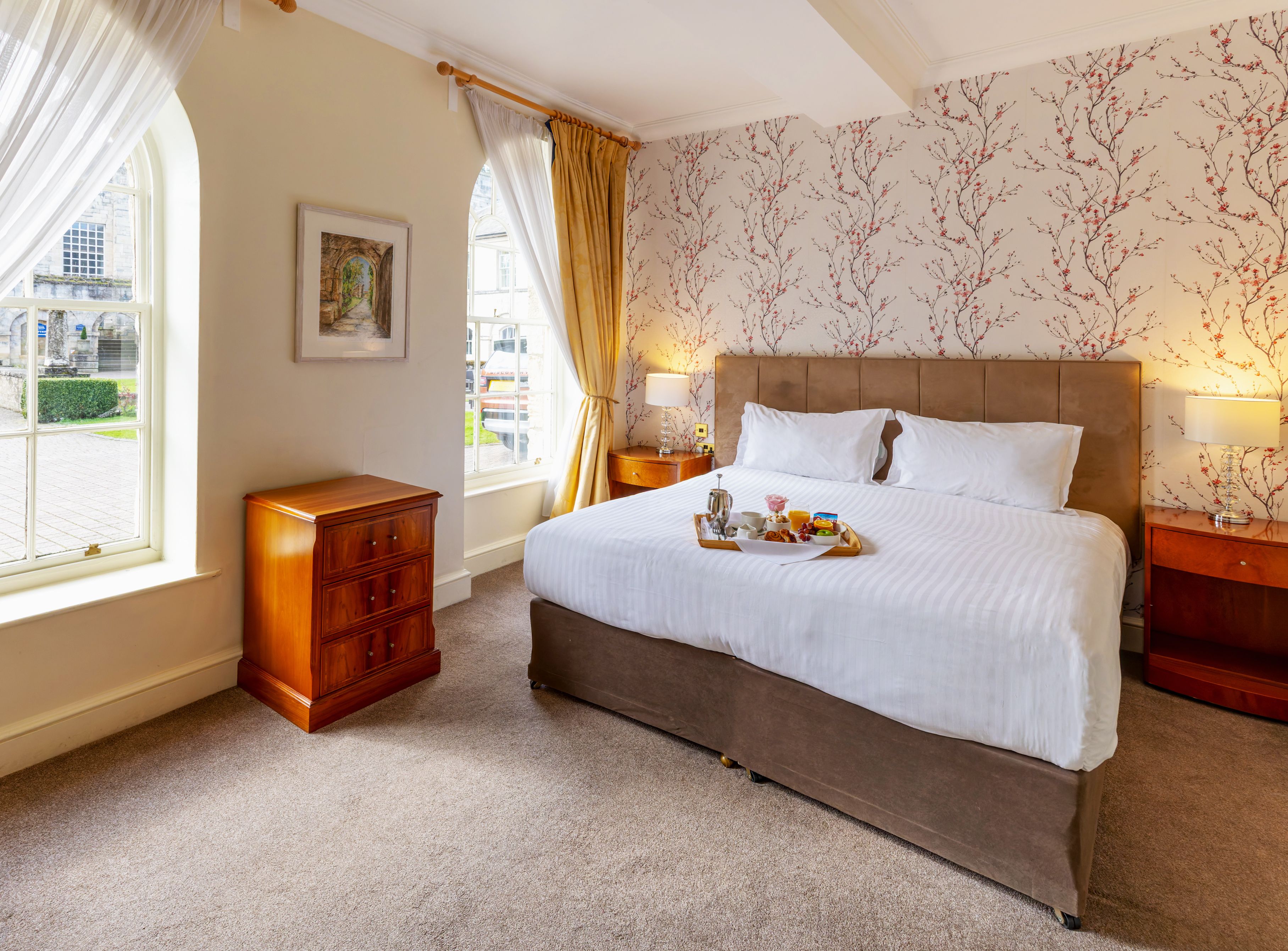 Bright and cozy hotel room with large windows, a double bed, and breakfast served on a tray.