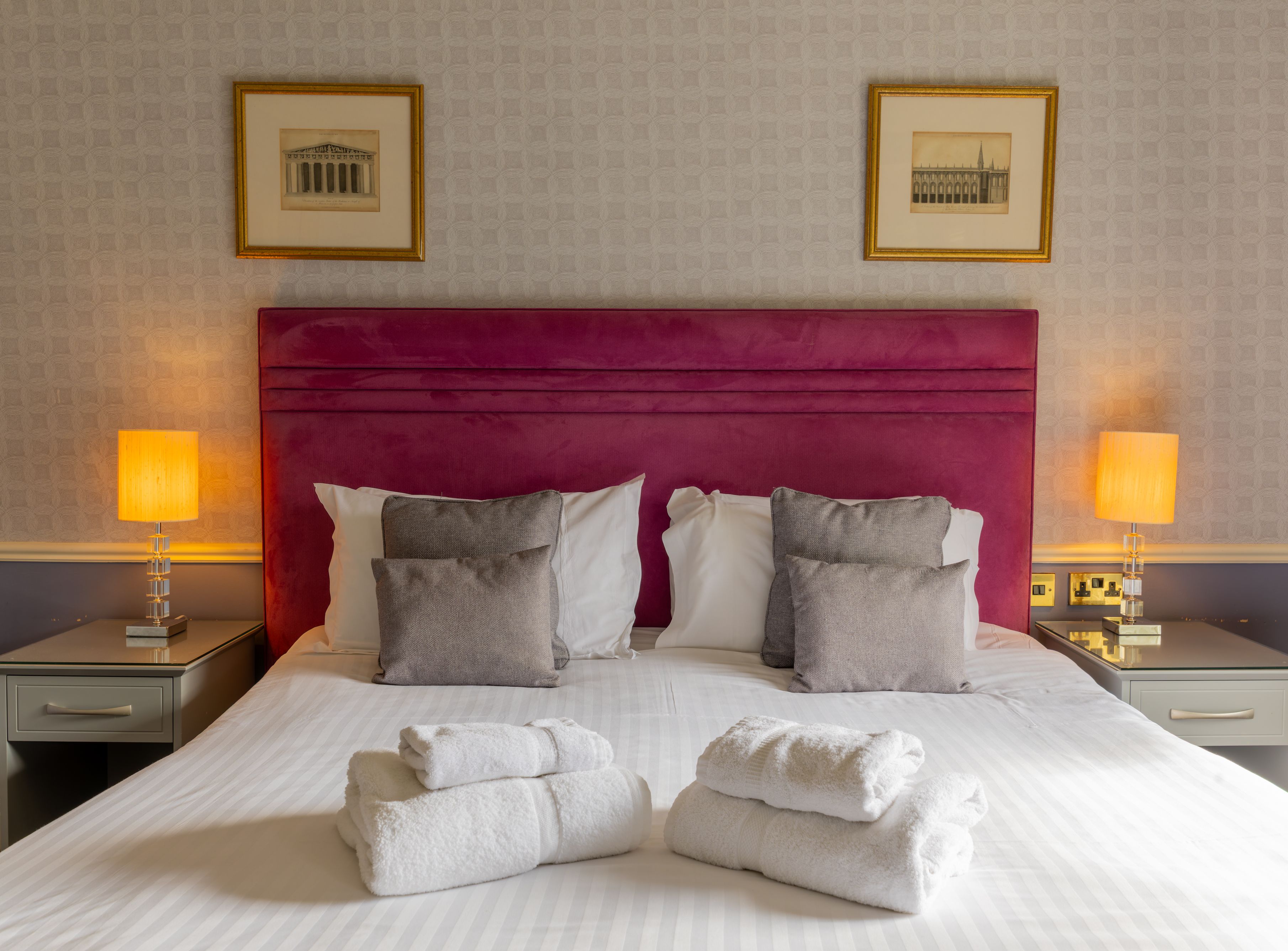Elegant hotel room with a large bed, purple headboard, neatly folded towels, and bedside lamps.