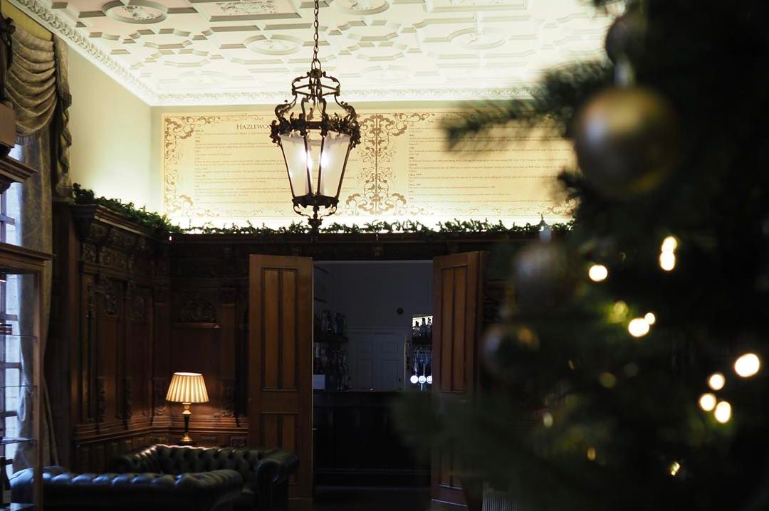 Elegant room with checkered floor, leather sofas, ornate wooden paneling, and a decorated Christmas tree in the foreground.