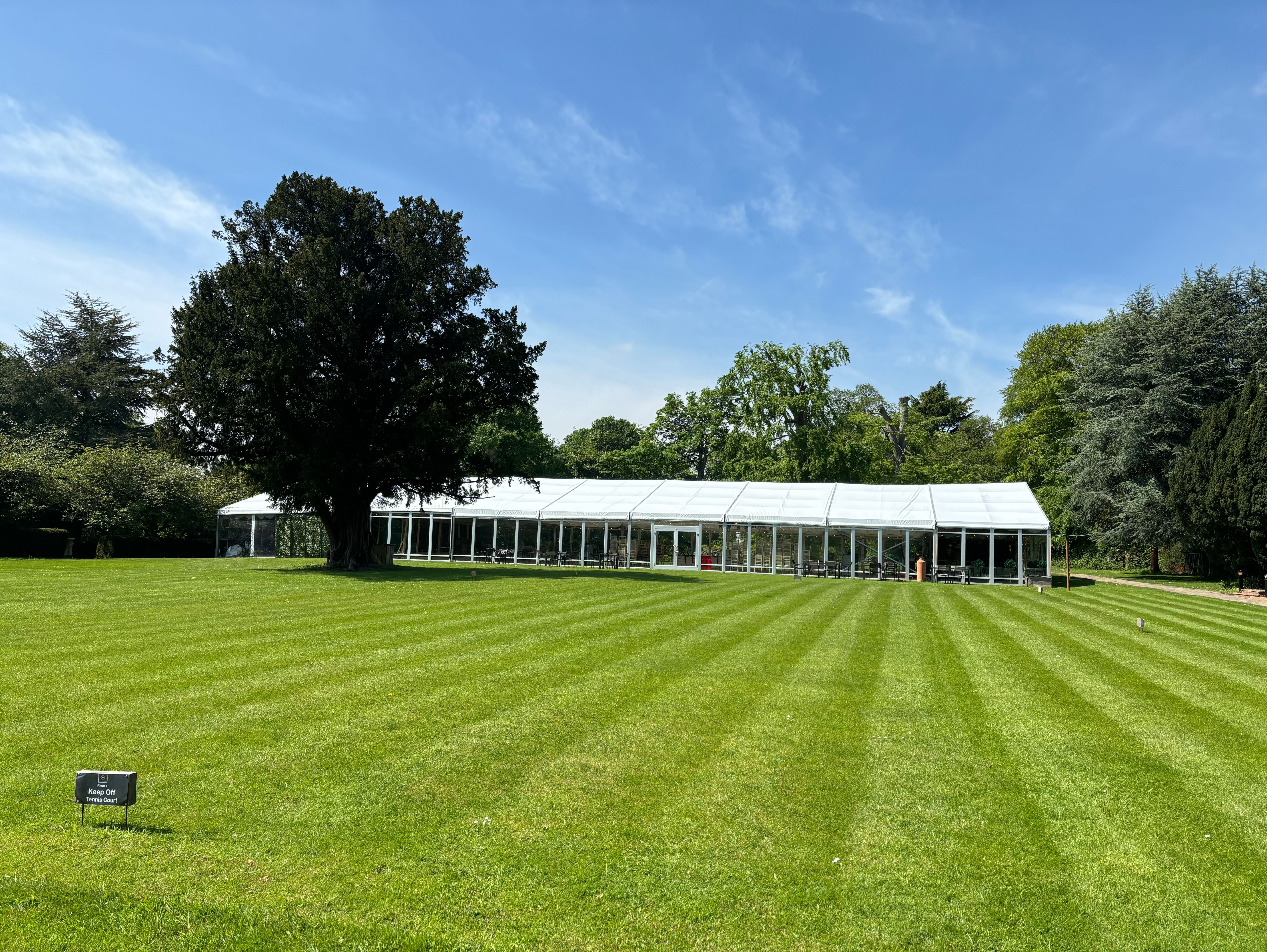 Large white marquee on a well-manicured lawn with trees and blue sky