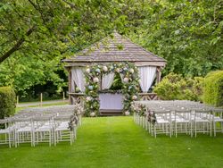 Outdoor wedding ceremony setup with rows of white chairs facing a gazebo decorated with floral arrangements