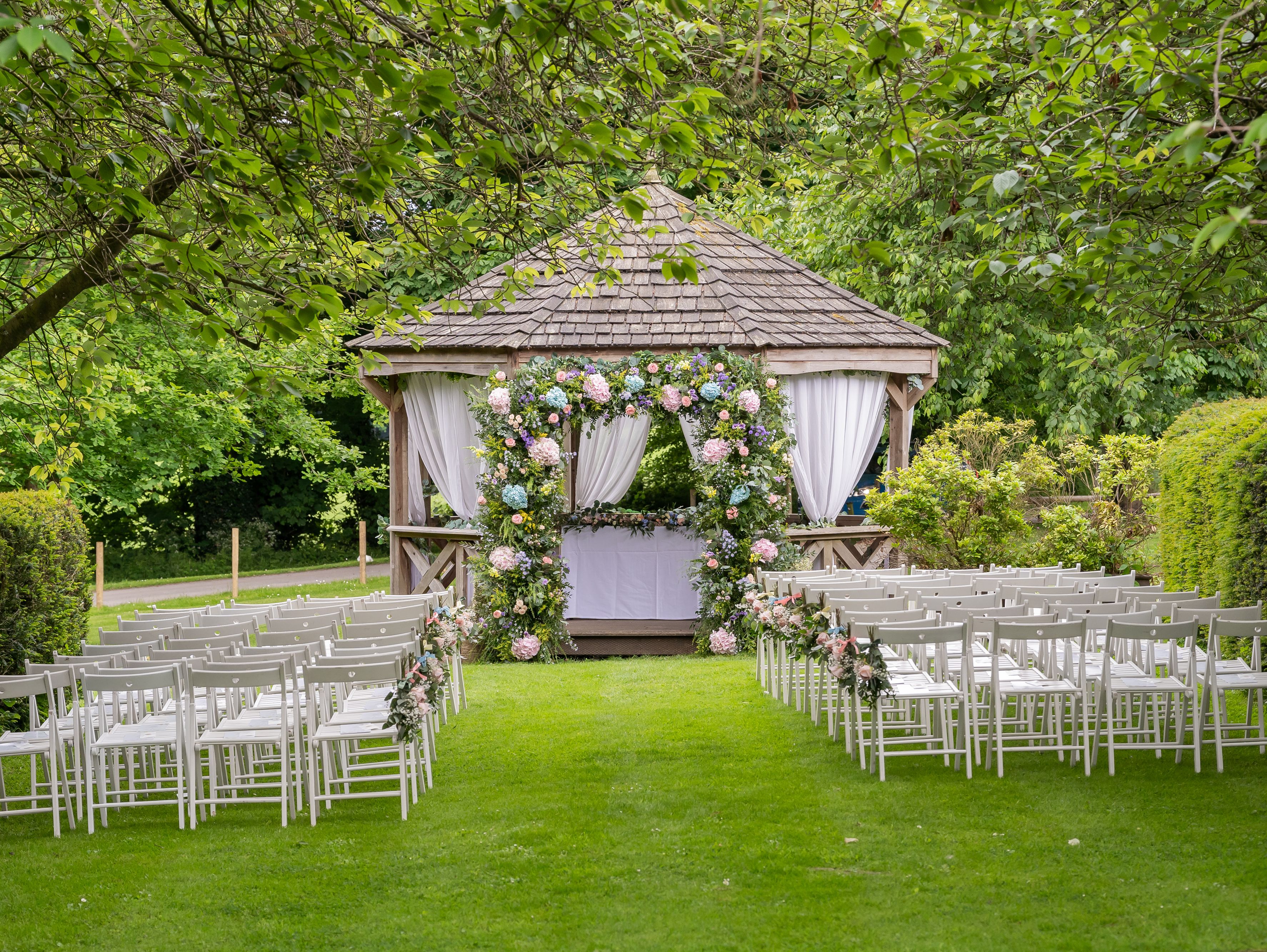 Outdoor wedding ceremony setup with rows of white chairs facing a gazebo decorated with floral arrangements