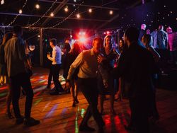 People dancing and socializing at a lively indoor party with colorful lights and hanging string lights.