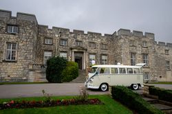 Classic white van decorated for a wedding parked in front of a historic stone castle
