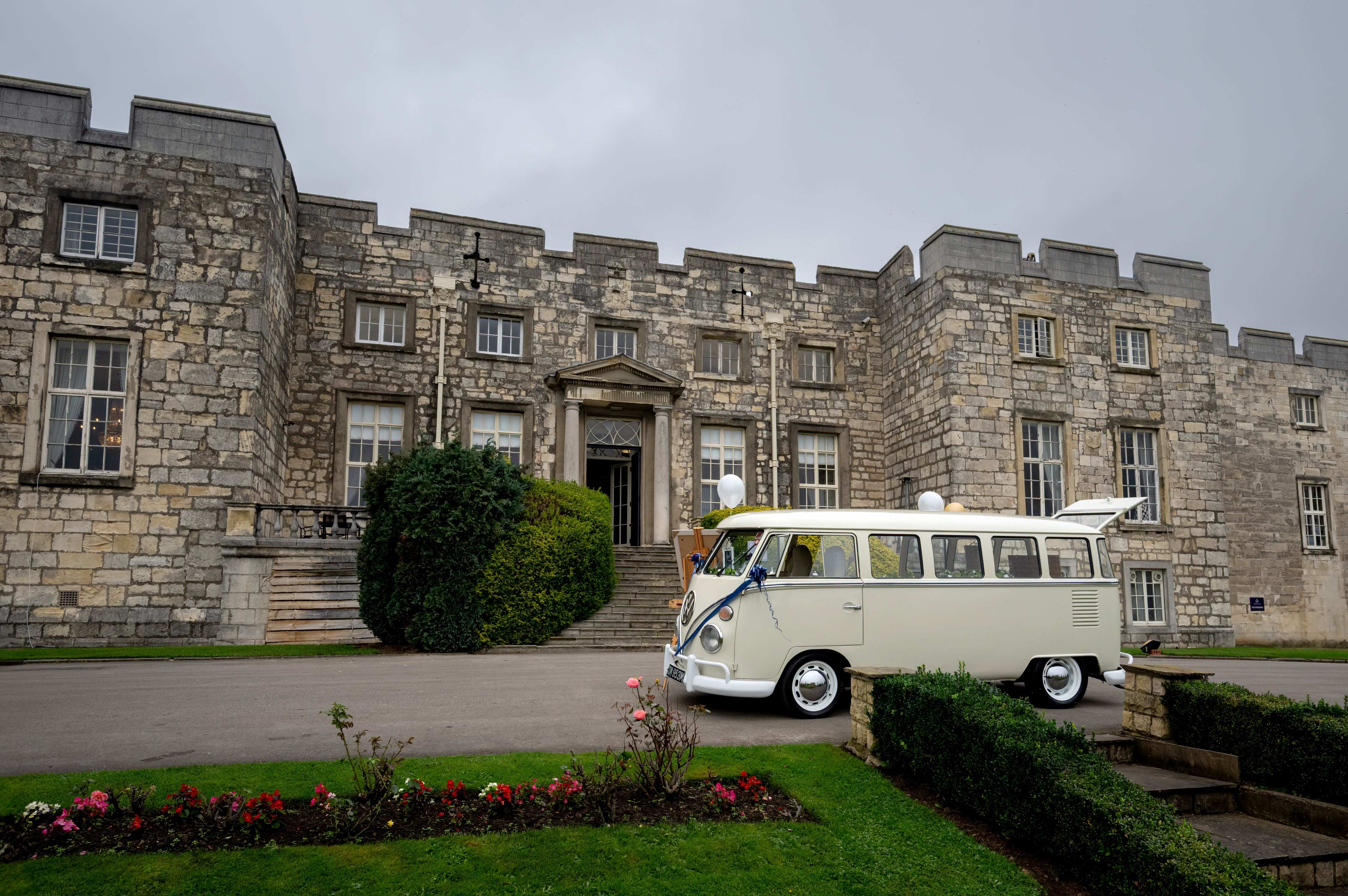 Classic white van decorated for a wedding parked in front of a historic stone castle