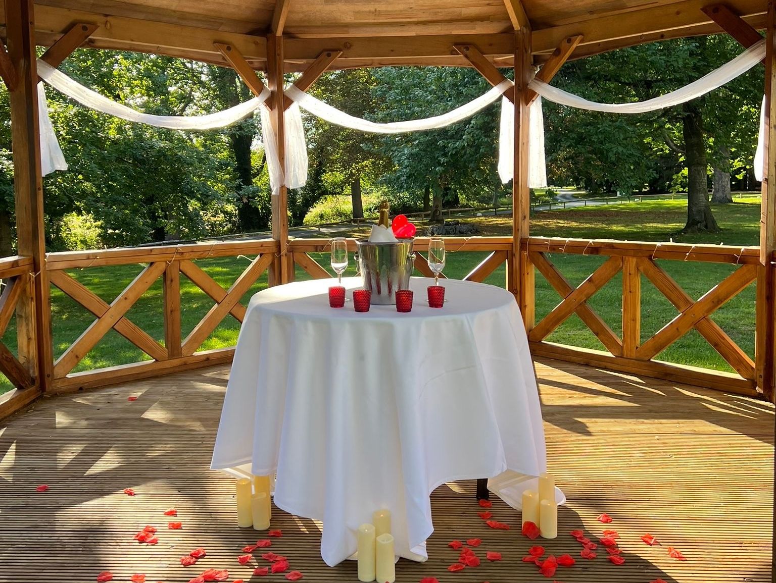 Romantic table setup with candles and rose petals under a wooden garden pagoda