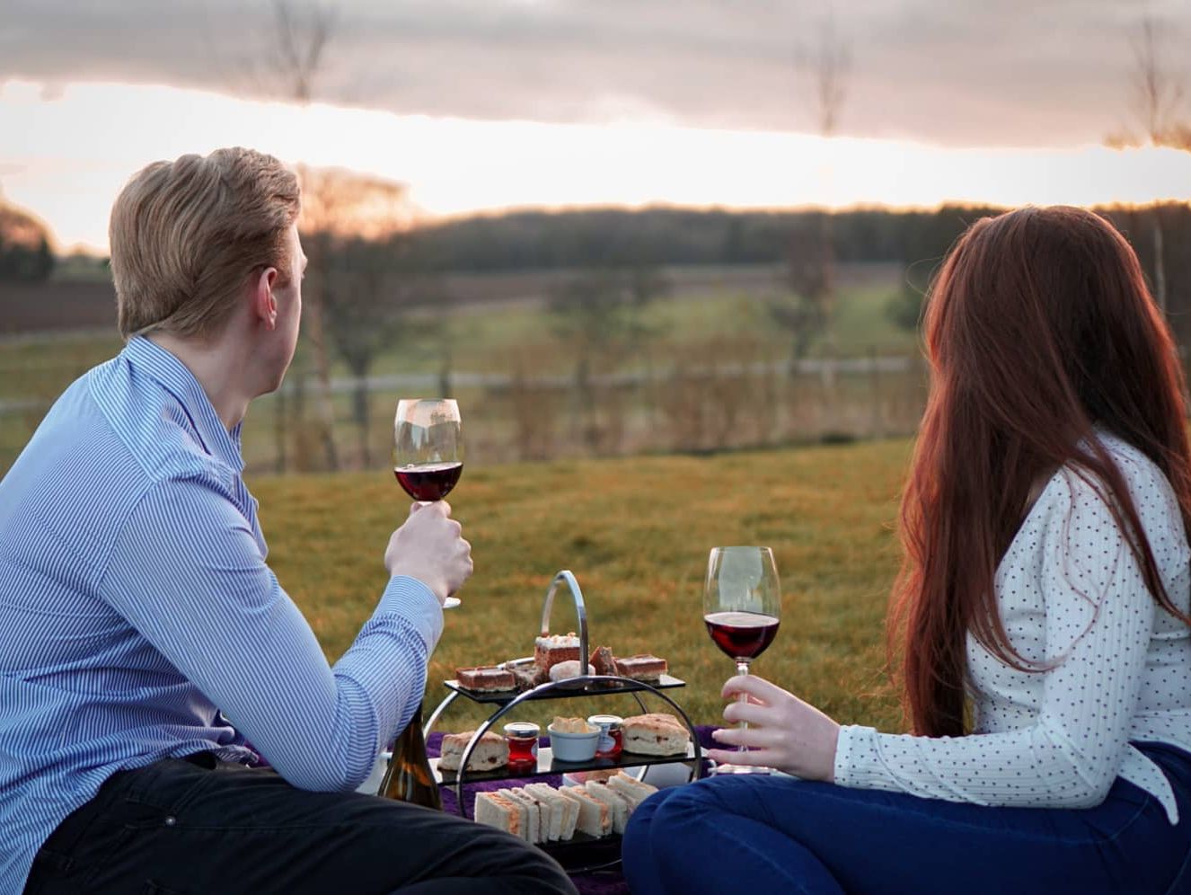 Couple enjoying wine and snacks at a picnic on a lawn during sunset