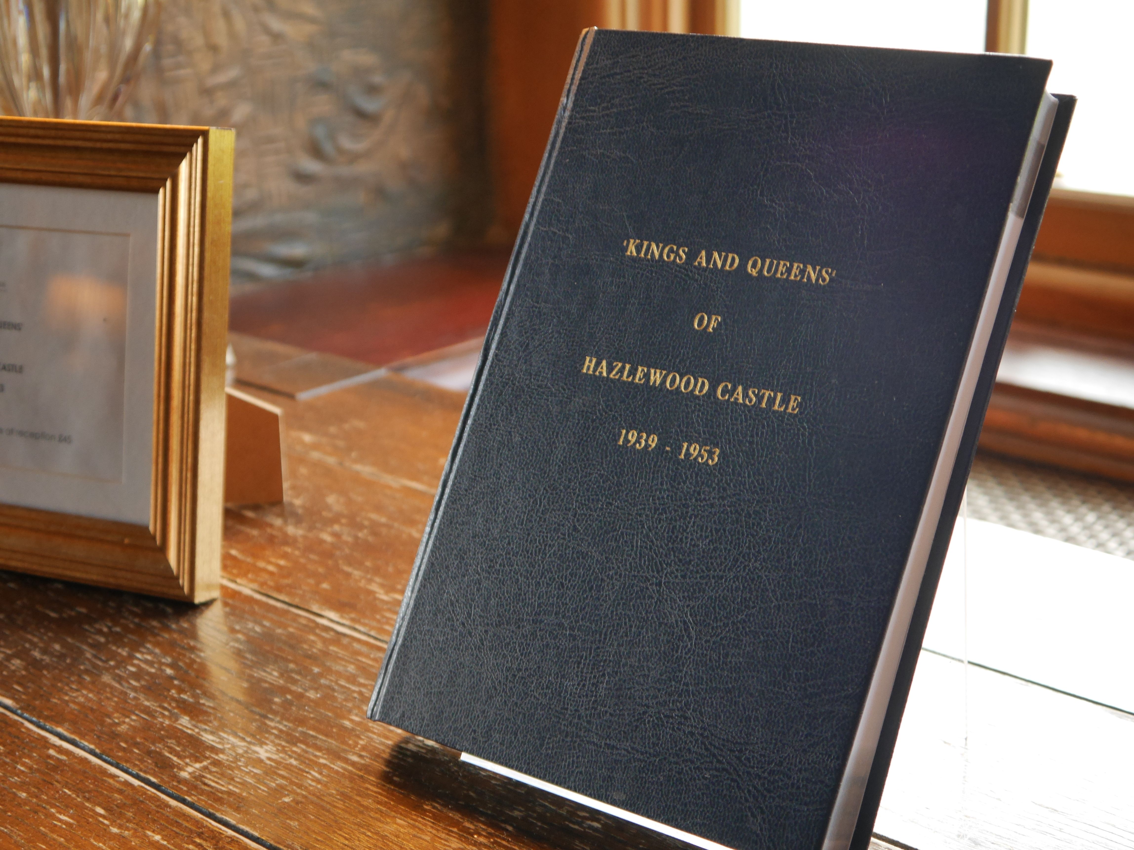 A book titled 'Kings and Queens of Hazlewood Castle 1939-1953' displayed on a wooden table near a framed picture.