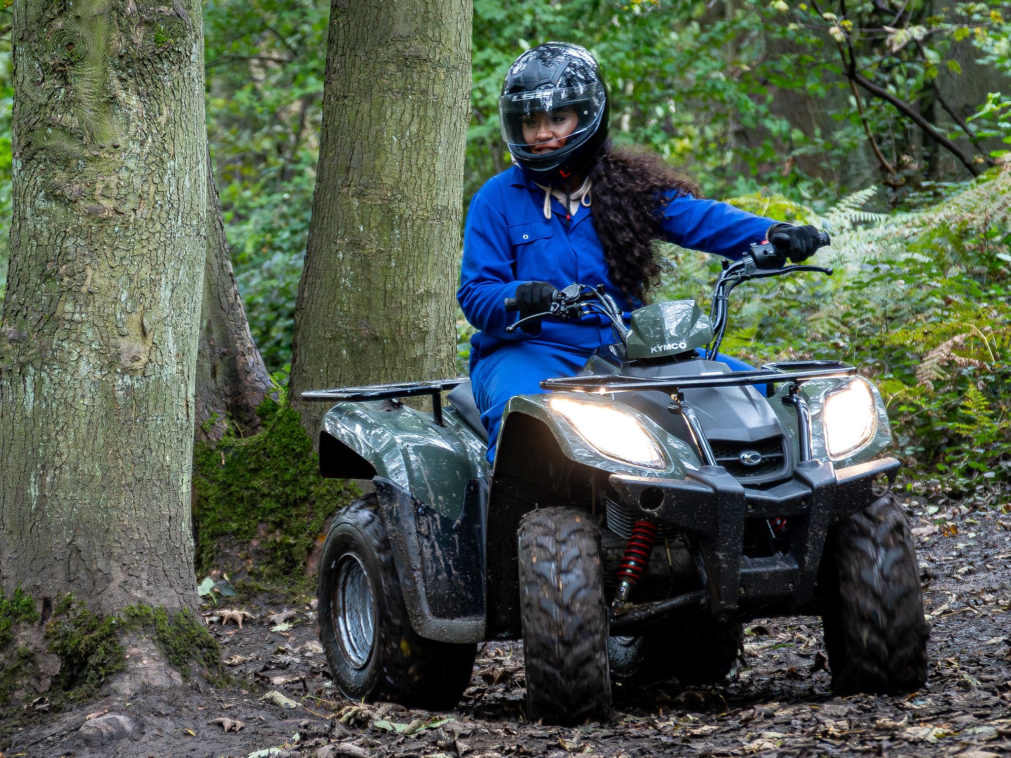 Person riding a quad bike through a forest trail.