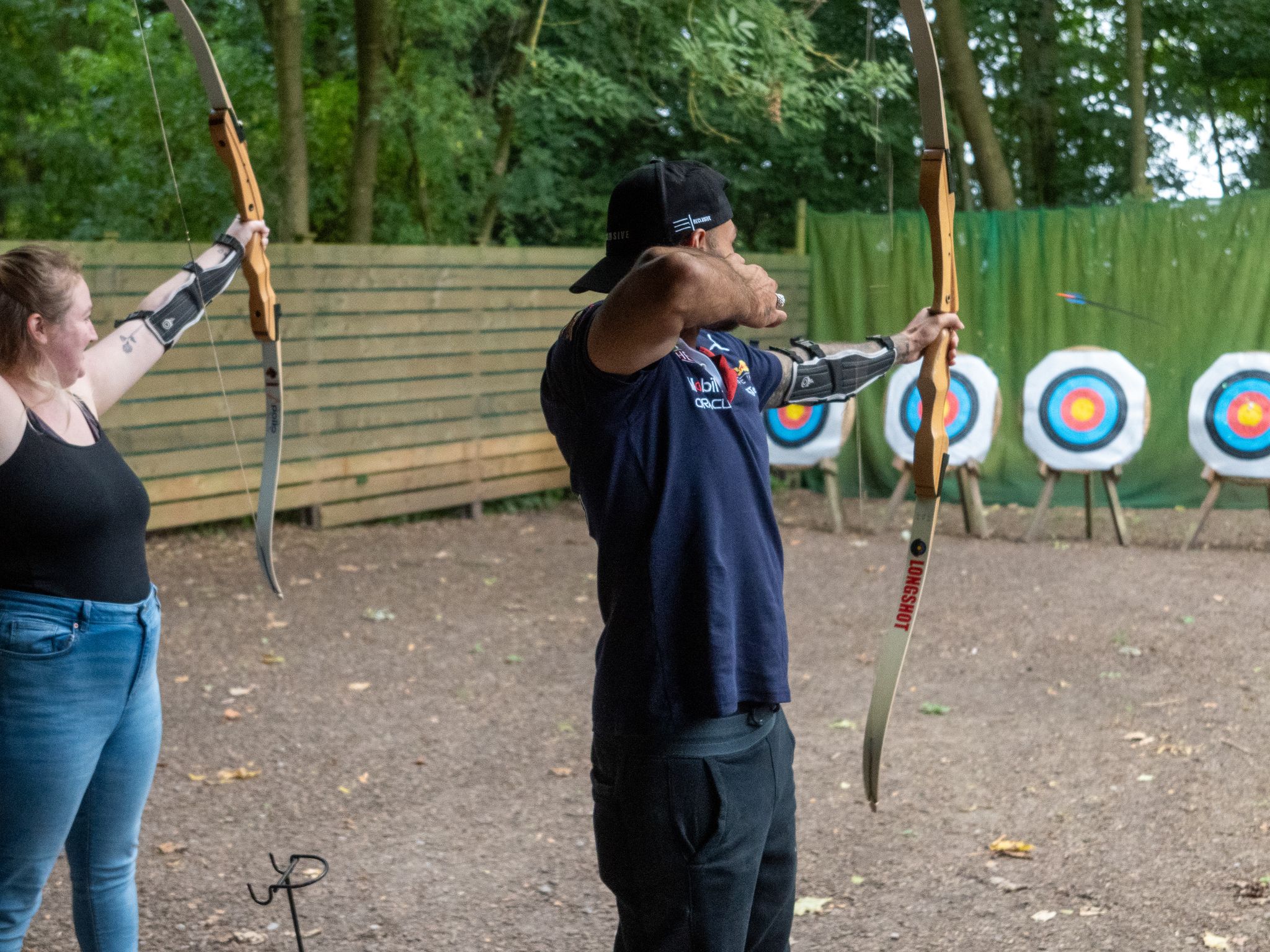 Two people practicing archery outdoors, aiming at target boards.