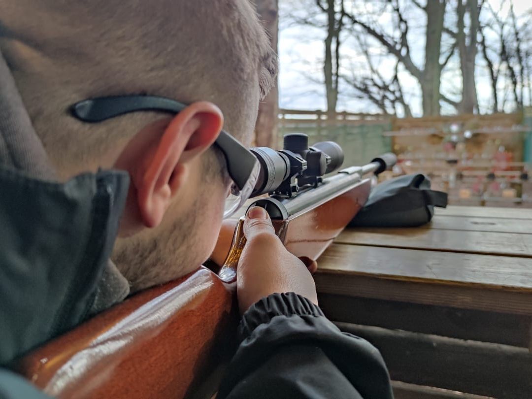 Person aiming a scoped rifle at an outdoor shooting range