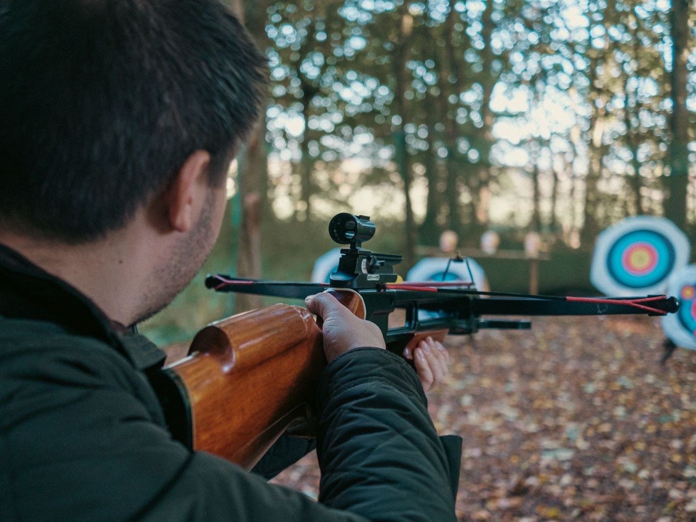 Person aiming a crossbow at archery targets in a wooded outdoor setting