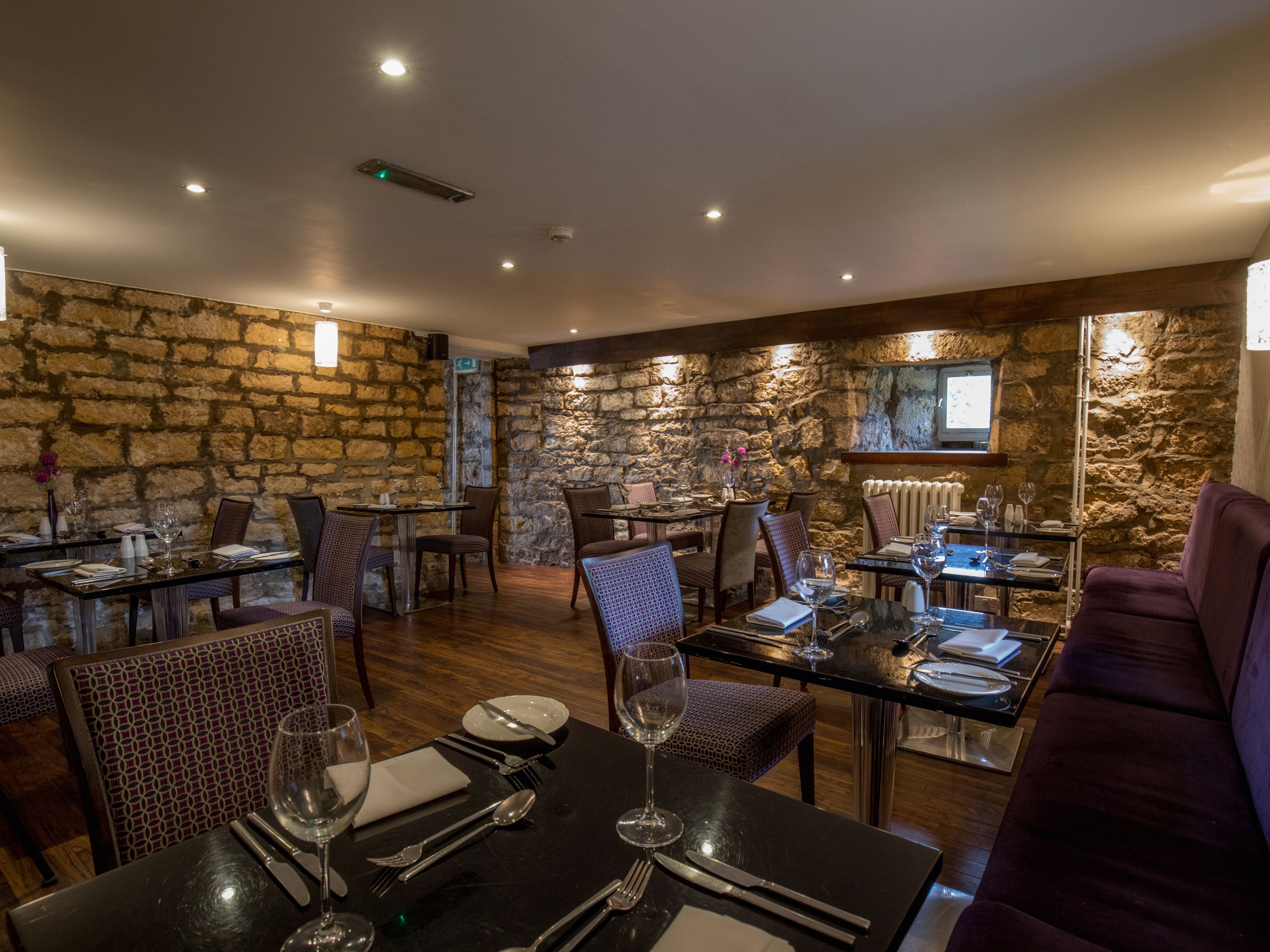 Cozy restaurant interior with stone walls, set tables, and purple cushioned seating