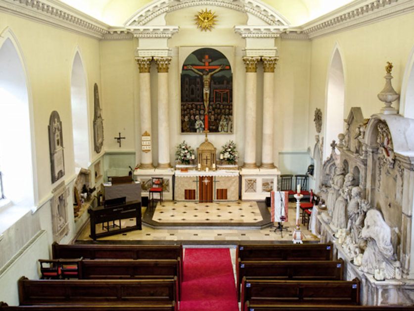 Interior of a chapel with wooden pews, a red carpet, an altar, organ, marble columns, and ornate sculptures on the walls.