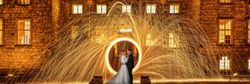 Bride and groom standing in front of a stone building at night, surrounded by a captivating display of swirling golden sparklers.