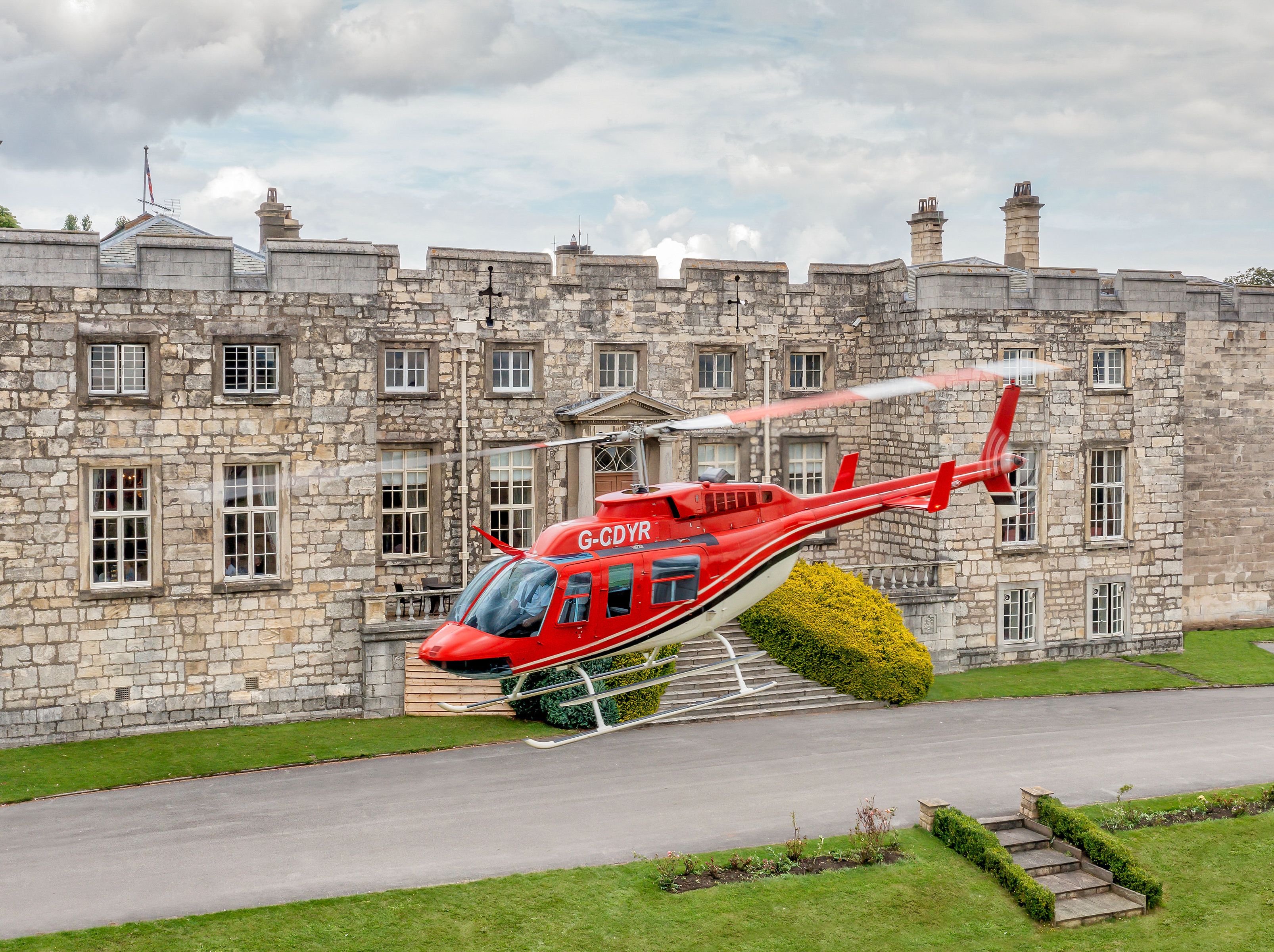 Red helicopter hovering in front of a historic stone building.
