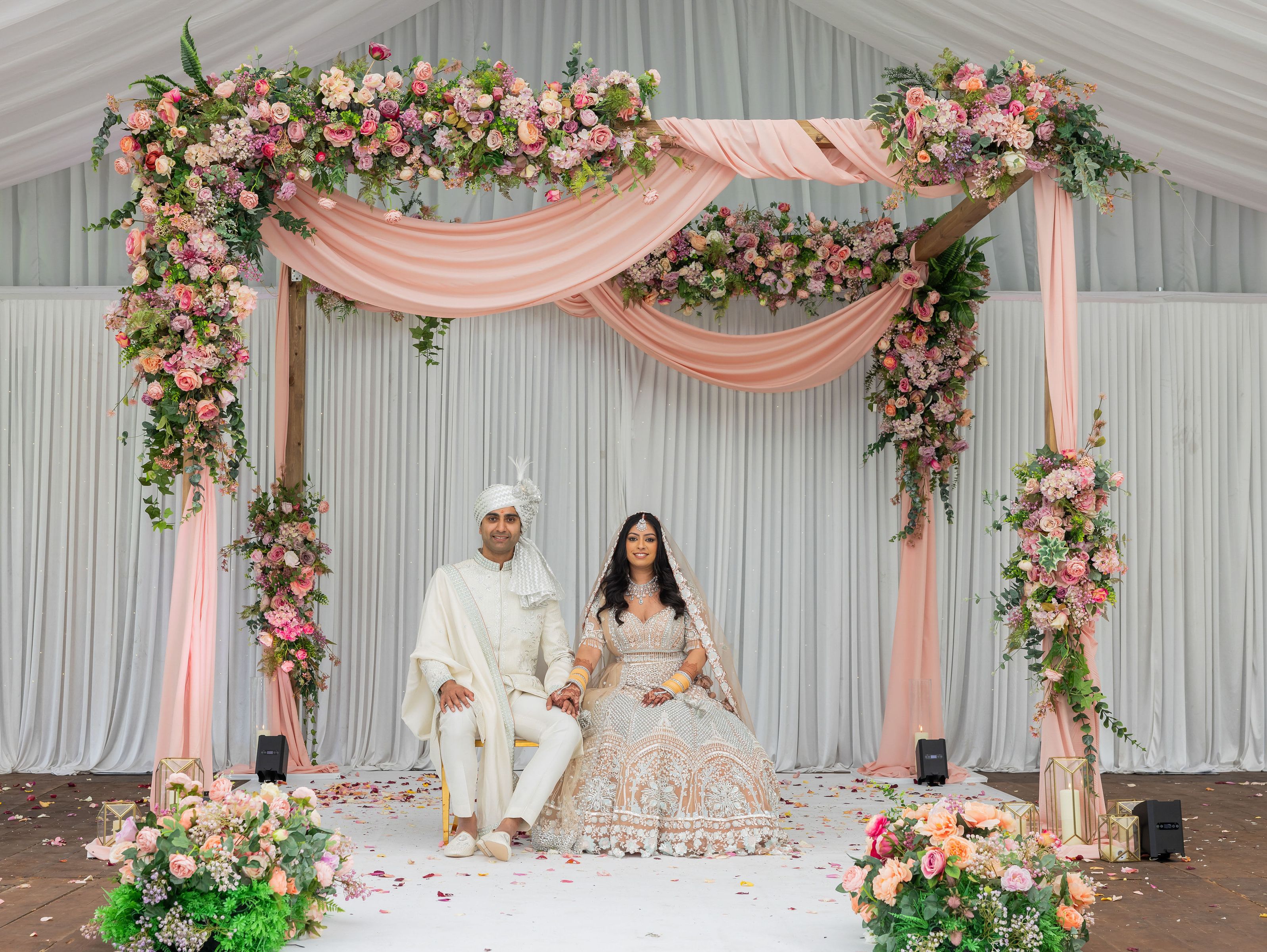 Bride and groom in traditional attire sitting under a floral wedding arch