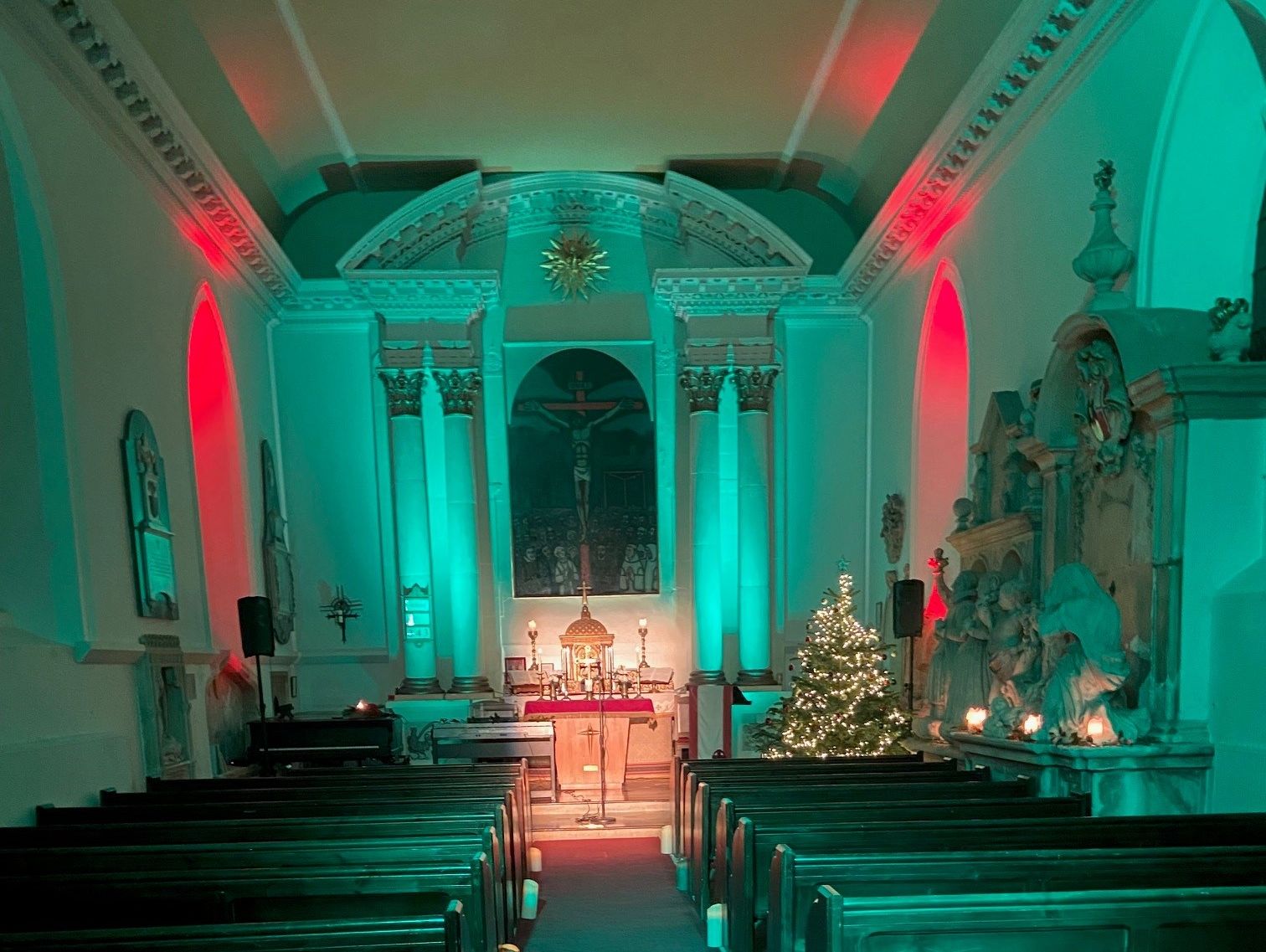 Church interior decorated for Christmas with candle lights and a lit Christmas tree near the altar.