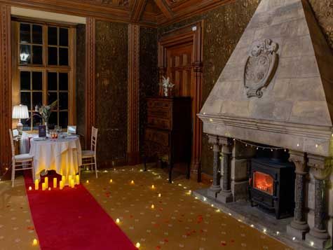 Romantic dinner setup in a grand room with a fireplace, red carpet, and candles.