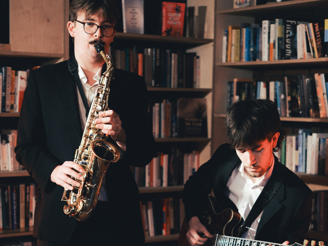 Saxophonist and guitarist performing bespoke jazz in front of bookshelves
