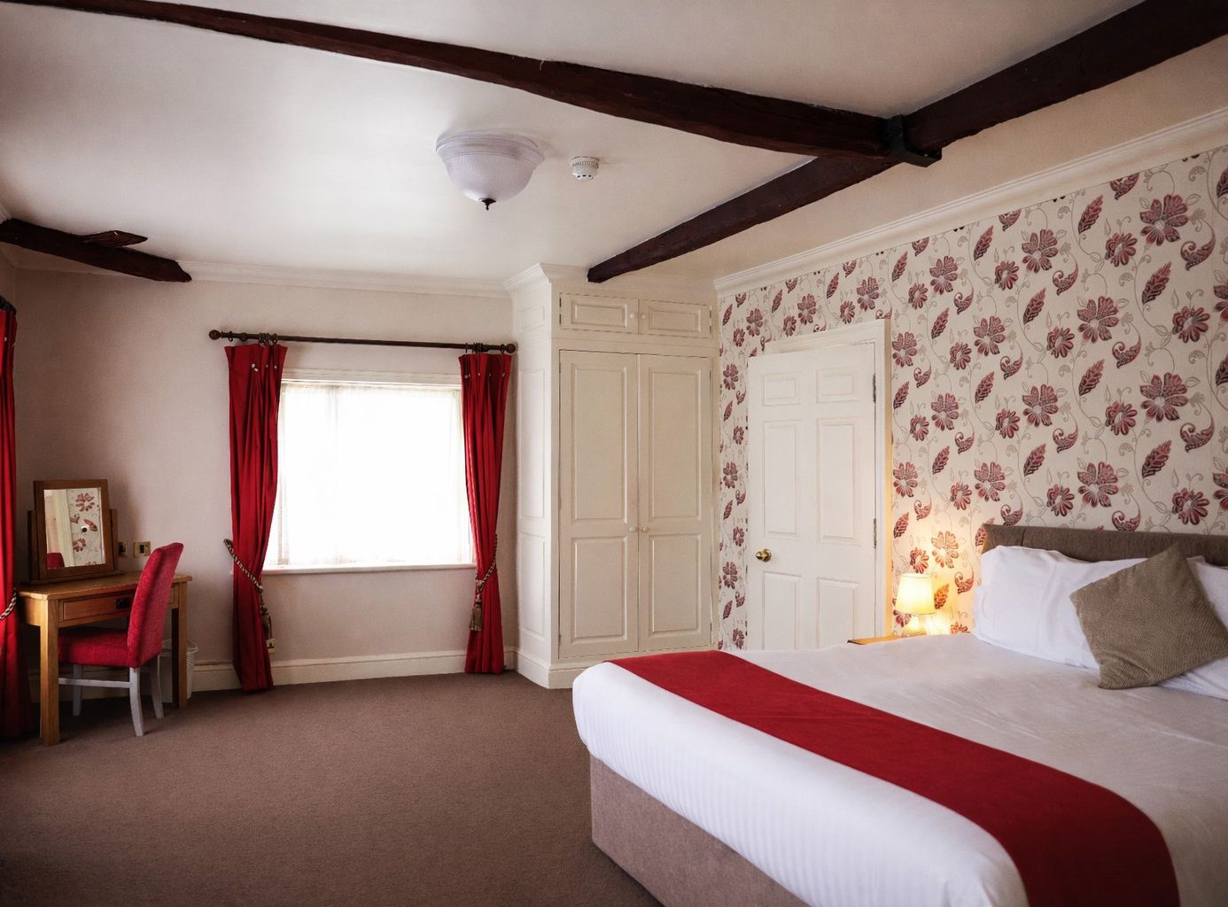 Cosy bedroom with red curtains, patterned feature wall, and double bed with a red runner