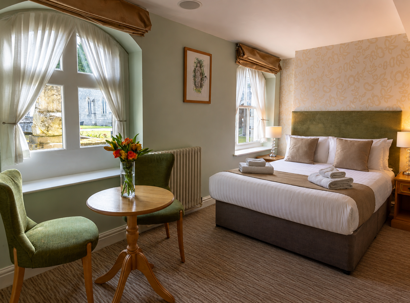 Cosy hotel bedroom with double bed, bedside lamps, arched window and small table with flowers