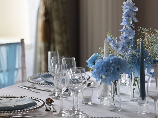 Elegantly set dining table with blue floral centrepieces, glassware and silver cutlery