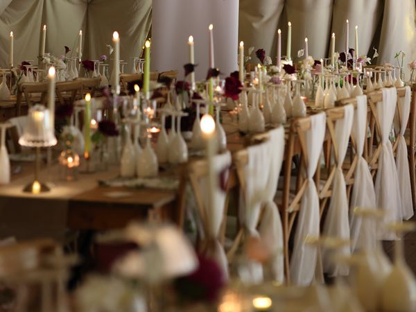 Long banquet tables with candles and small flower vases set in a draped marquee