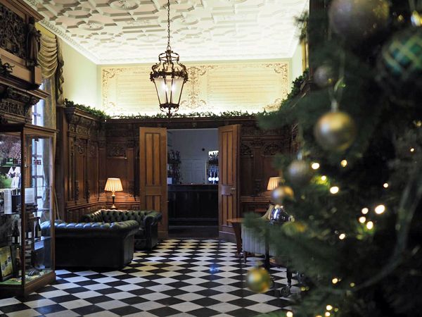 Ornate foyer with black-and-white chequered floor, leather sofa, chandelier and a decorated Christmas tree in the foreground