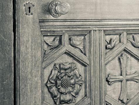 Close-up of an ornate wooden door with carved floral and cross motifs, showing a keyhole and decorative metal knob.