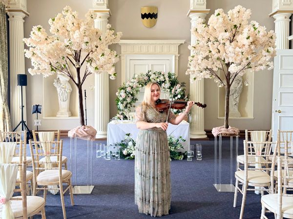 Violinist performing at an indoor wedding ceremony with floral arch and blossom trees