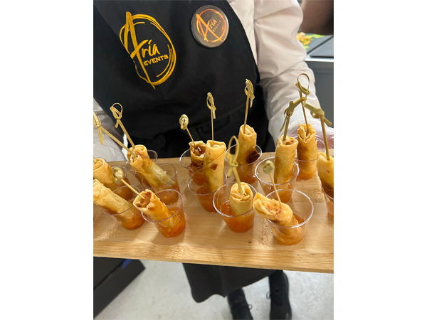 Server holding a wooden tray of bite-sized spring rolls in small cups with dipping sauce